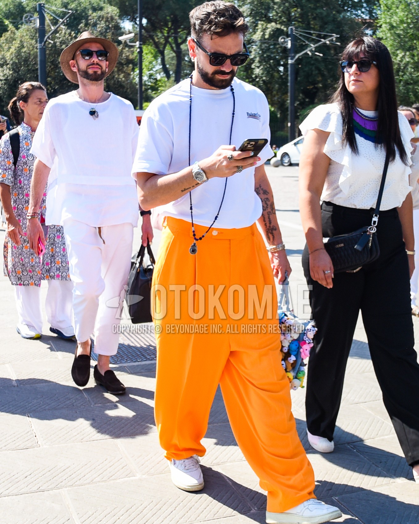 Men's spring summer outfit with black plain sunglasses, white one point t-shirt, orange plain slacks, orange plain wide pants, white low-cut sneakers.