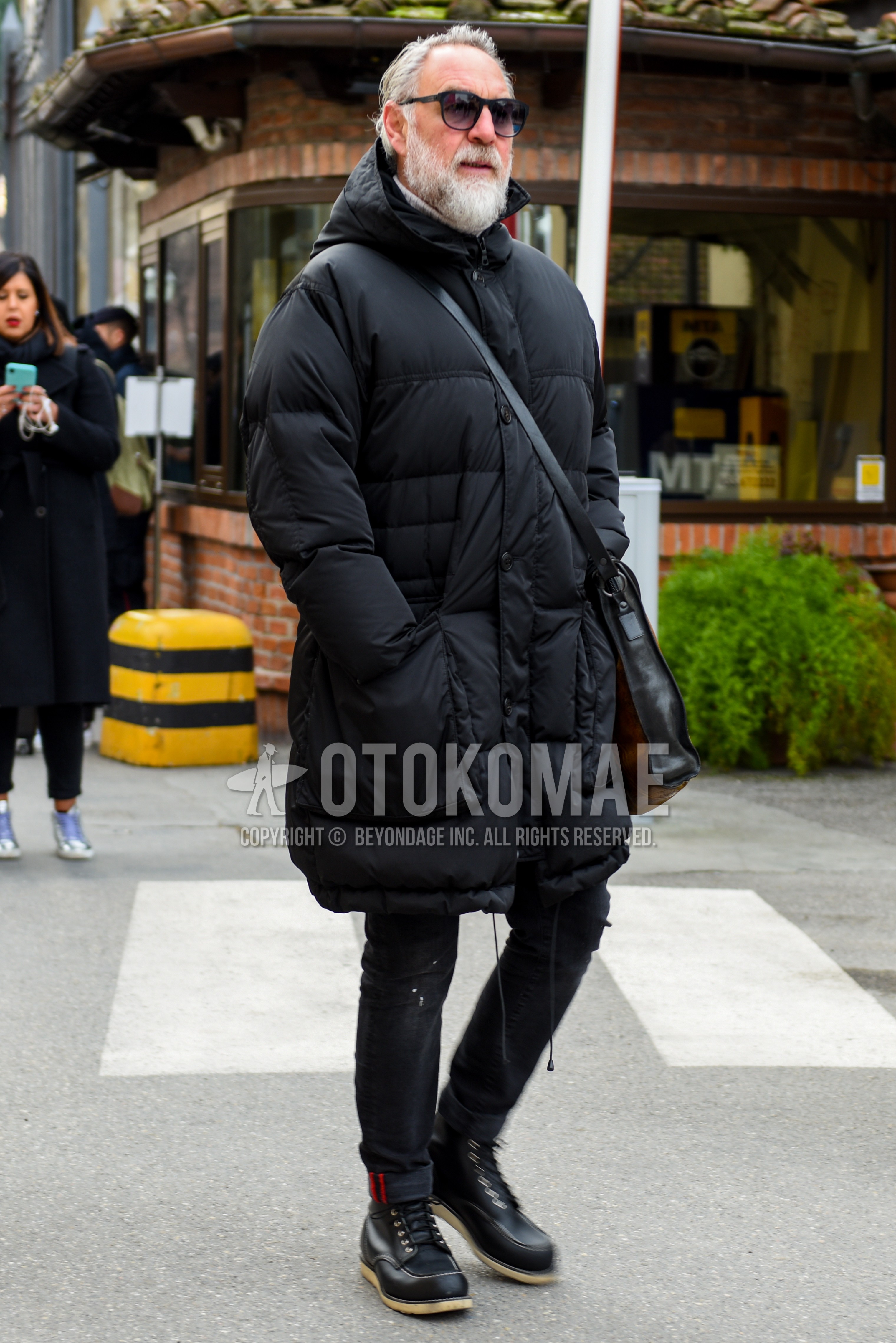 Men's autumn winter outfit with black plain sunglasses, black plain down jacket, black plain hooded coat, black plain denim/jeans, black work boots, black plain shoulder bag.