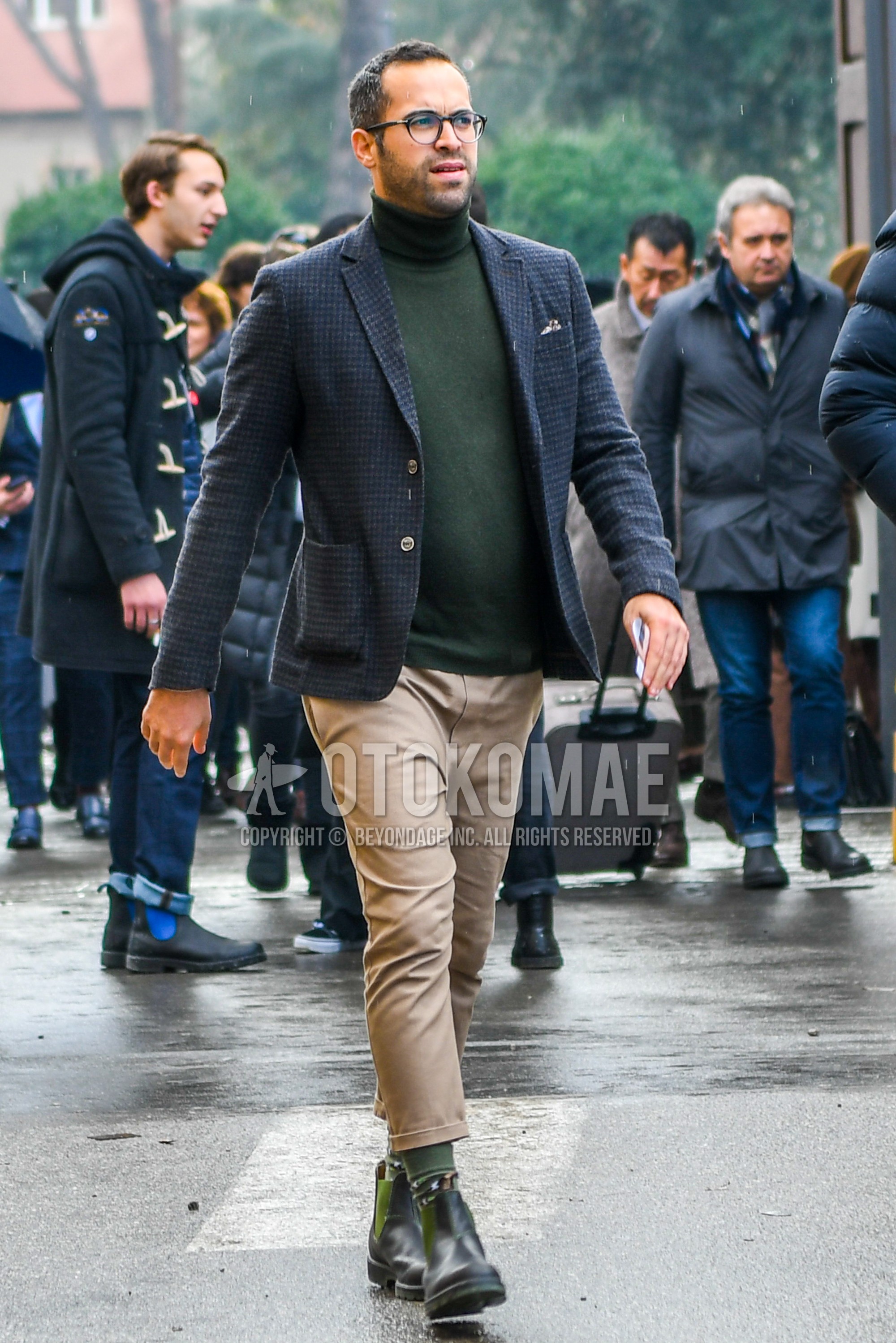 Men's winter outfit with plain glasses, dark gray check tailored jacket, olive green plain turtleneck knit, beige plain chinos, olive green plain socks, olive green side-gore boots.