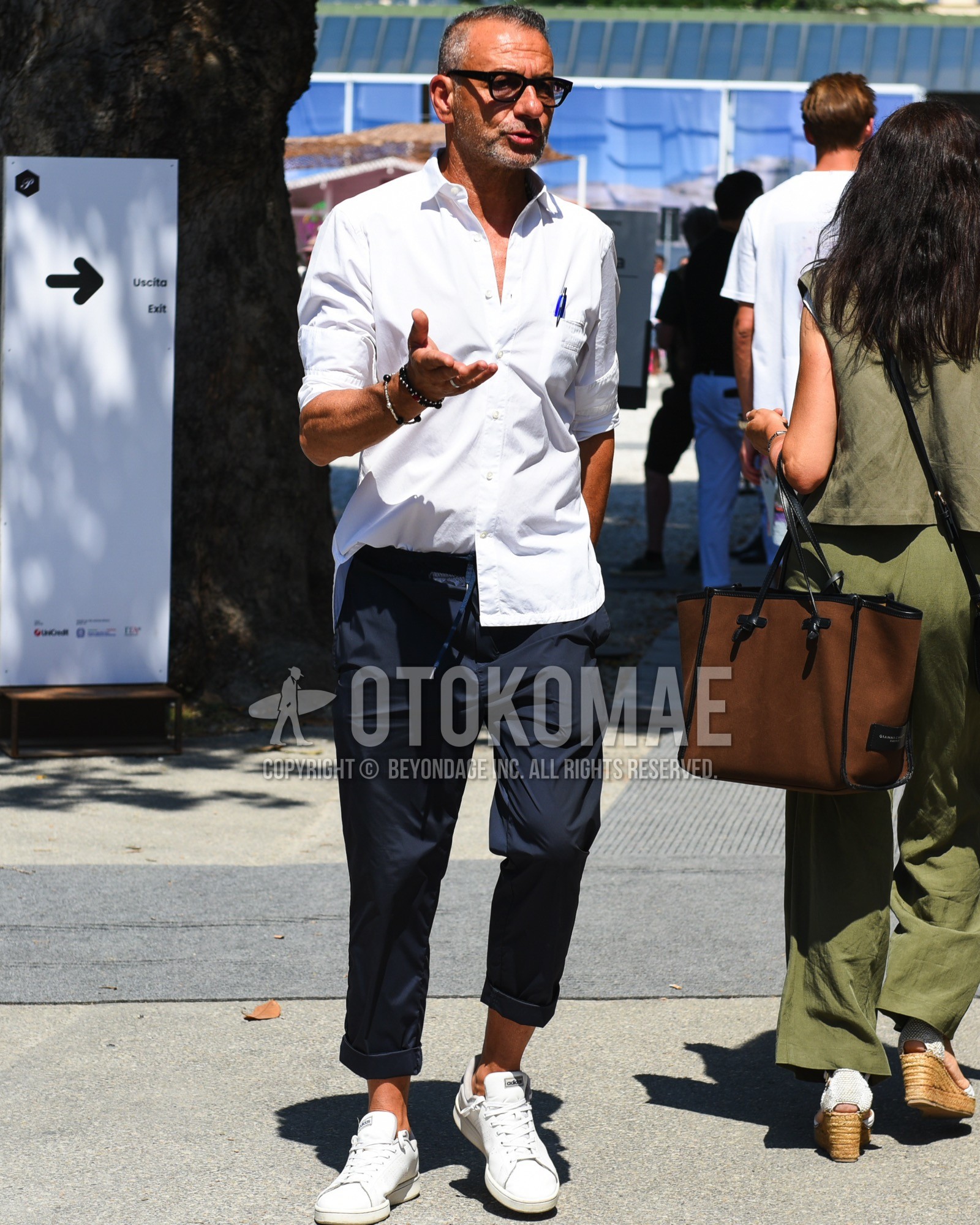 Men's spring summer outfit with black plain glasses, white one point shirt, navy plain easy pants, white low-cut sneakers.