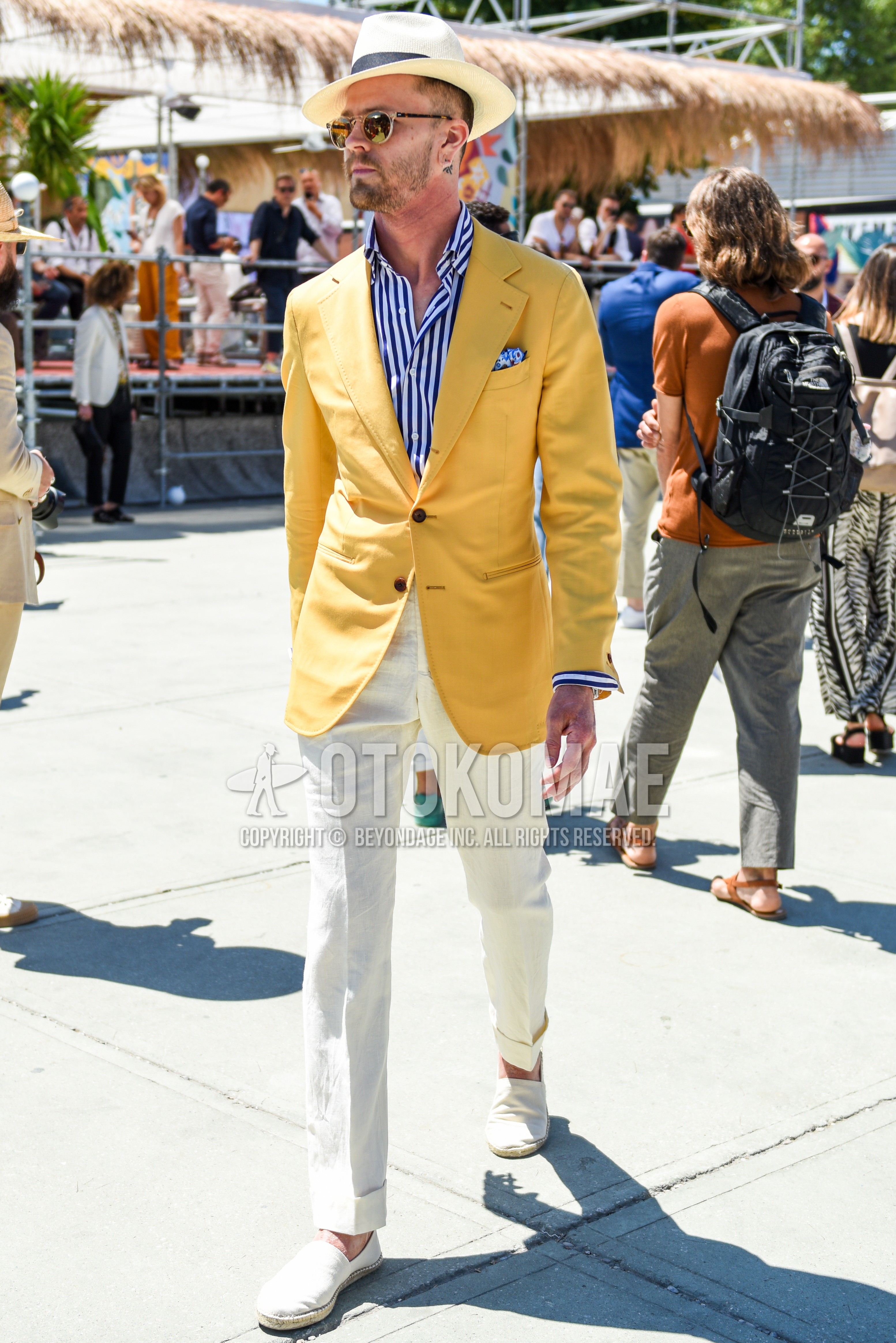 Men's spring summer outfit with beige plain hat, clear plain sunglasses, yellow plain tailored jacket, white blue stripes shirt, white plain slacks, white plain espadrille.