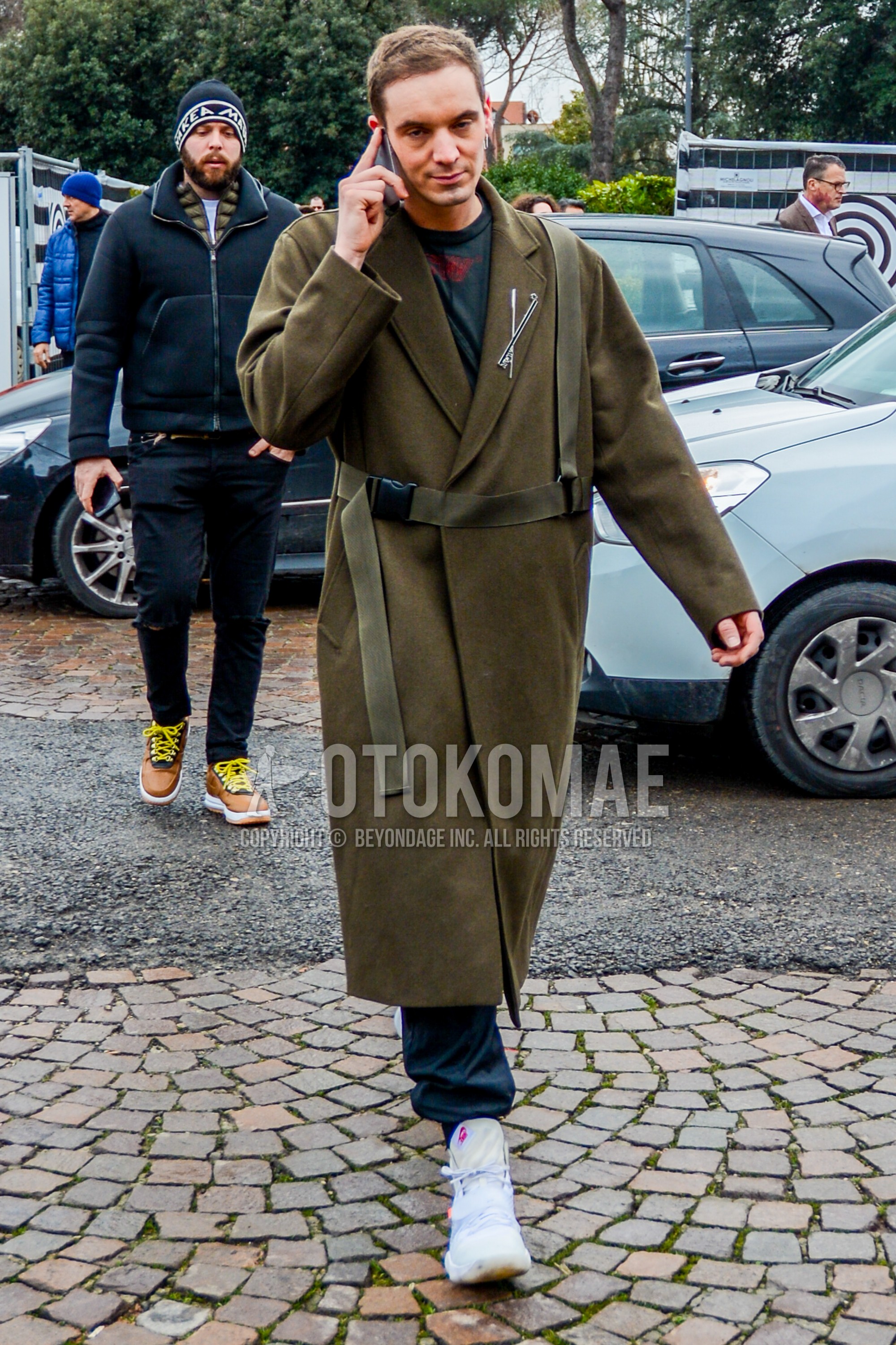 Men's autumn winter outfit with olive green plain belted coat, black one point t-shirt, white high-cut sneakers.
