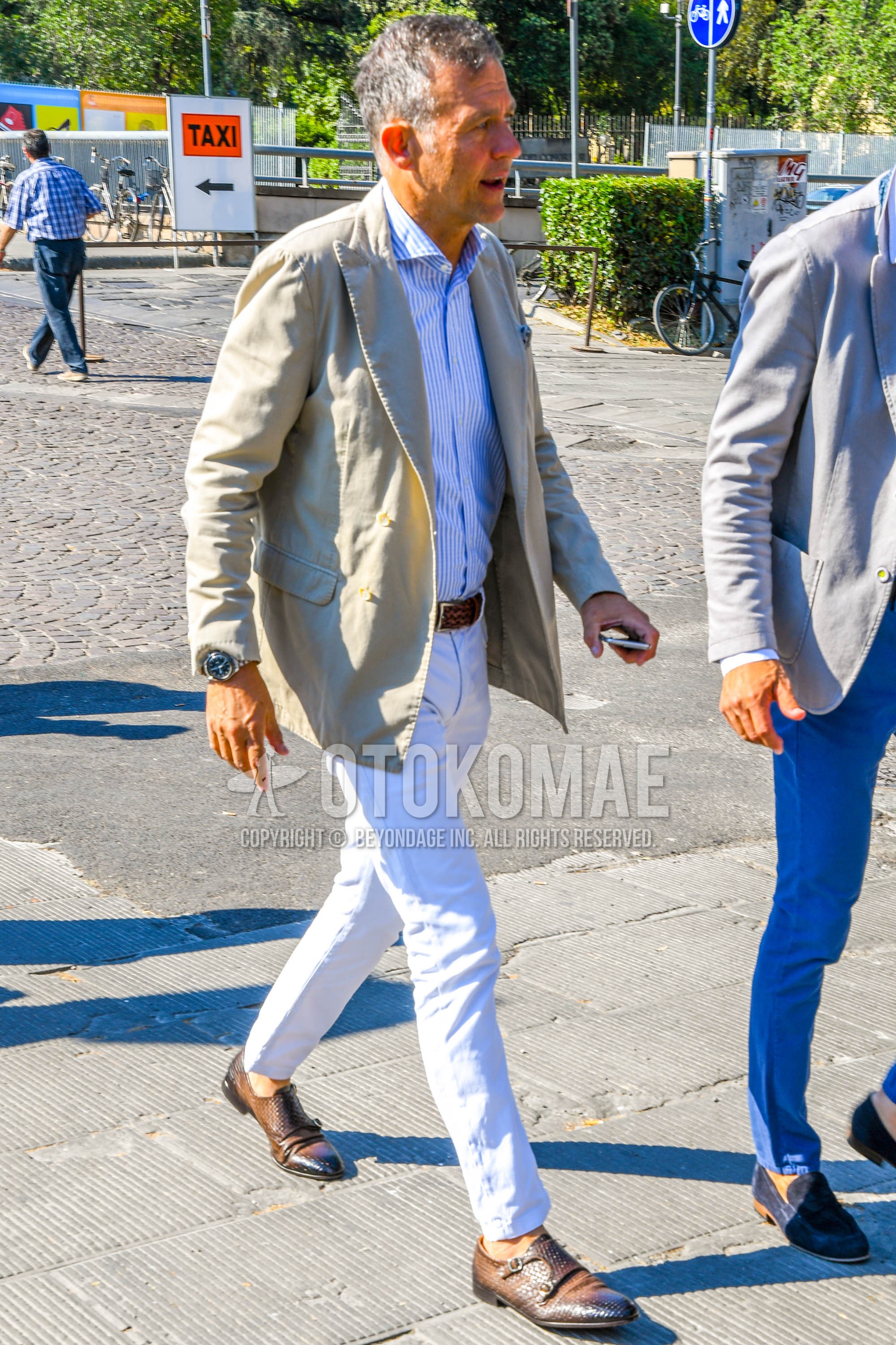 Men's spring summer outfit with beige plain tailored jacket, white light blue stripes shirt, brown plain braided belt, plain leather belt, white plain denim/jeans, brown monk shoes leather shoes.