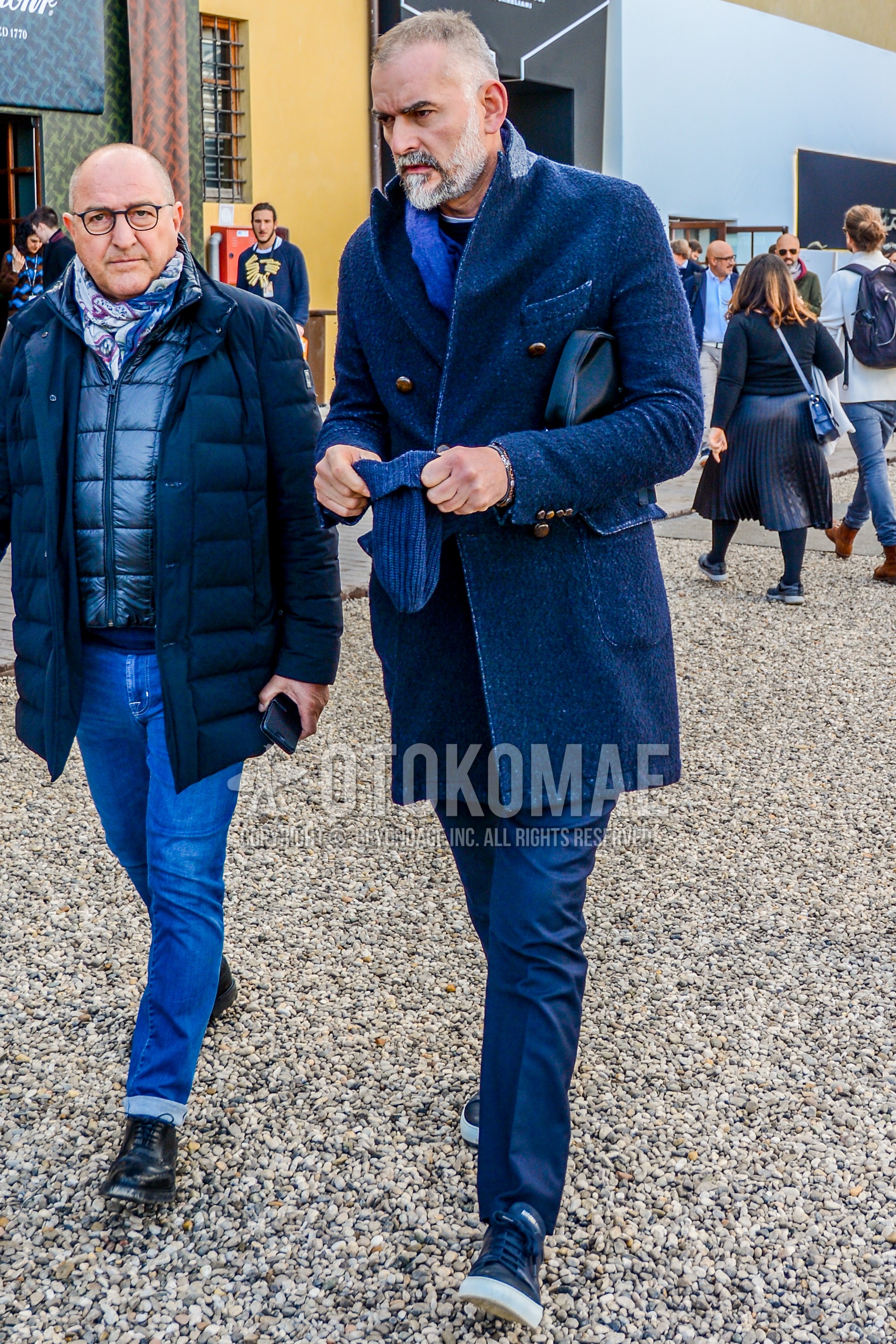 Men's autumn winter outfit with blue plain scarf, navy plain chester coat, gray plain slacks, black low-cut sneakers.