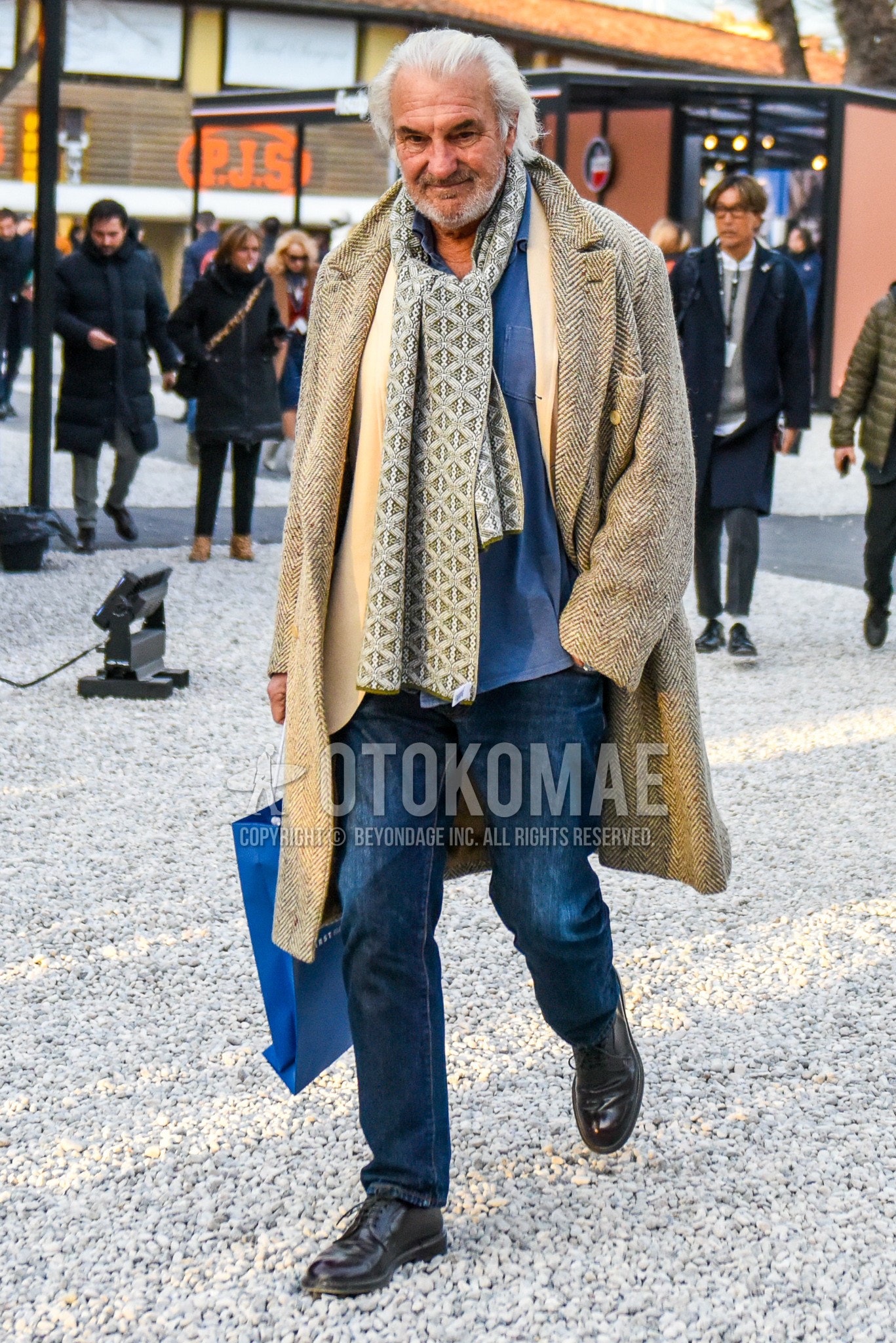 Men's autumn winter outfit with gray scarf scarf, beige herringbone chester coat, gray plain shirt, white plain tailored jacket, blue plain denim/jeans, brown straight-tip shoes leather shoes.