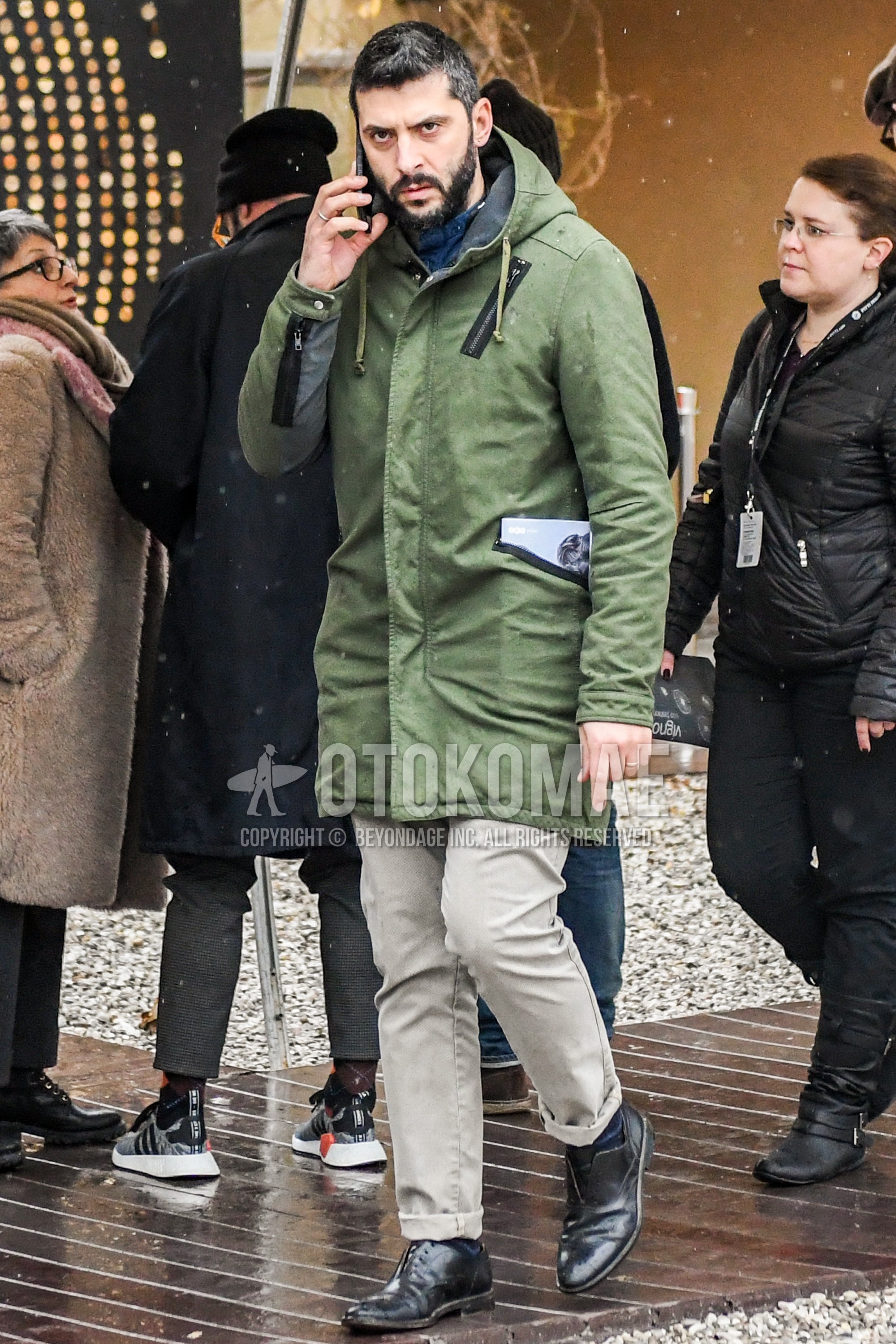 Men's autumn winter outfit with olive green plain hooded coat, beige plain chinos, black straight-tip shoes leather shoes.