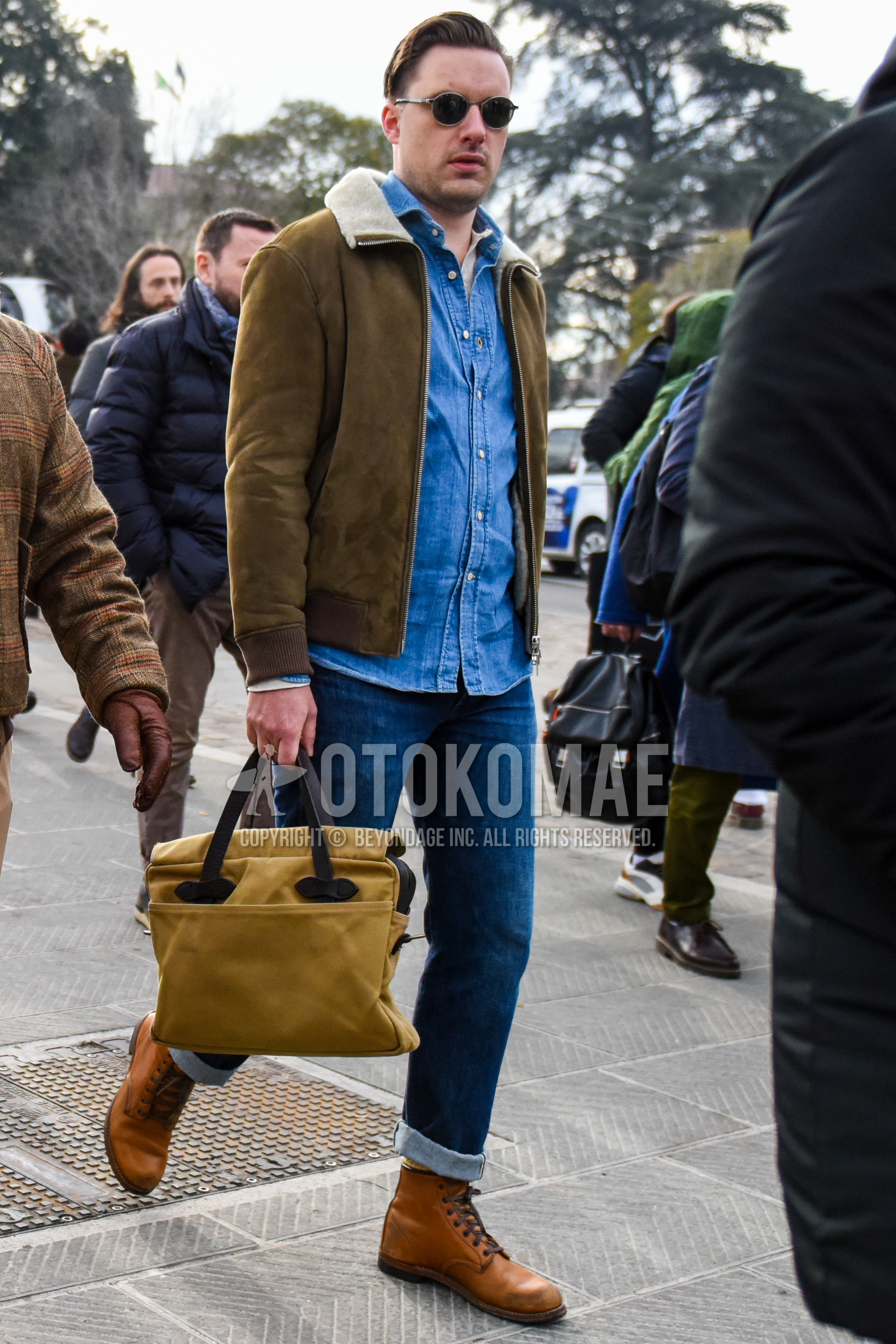 Men's autumn winter outfit with plain sunglasses, beige plain leather jacket, blue plain denim shirt/chambray shirt, blue plain denim/jeans, beige  boots, beige plain briefcase/handbag.