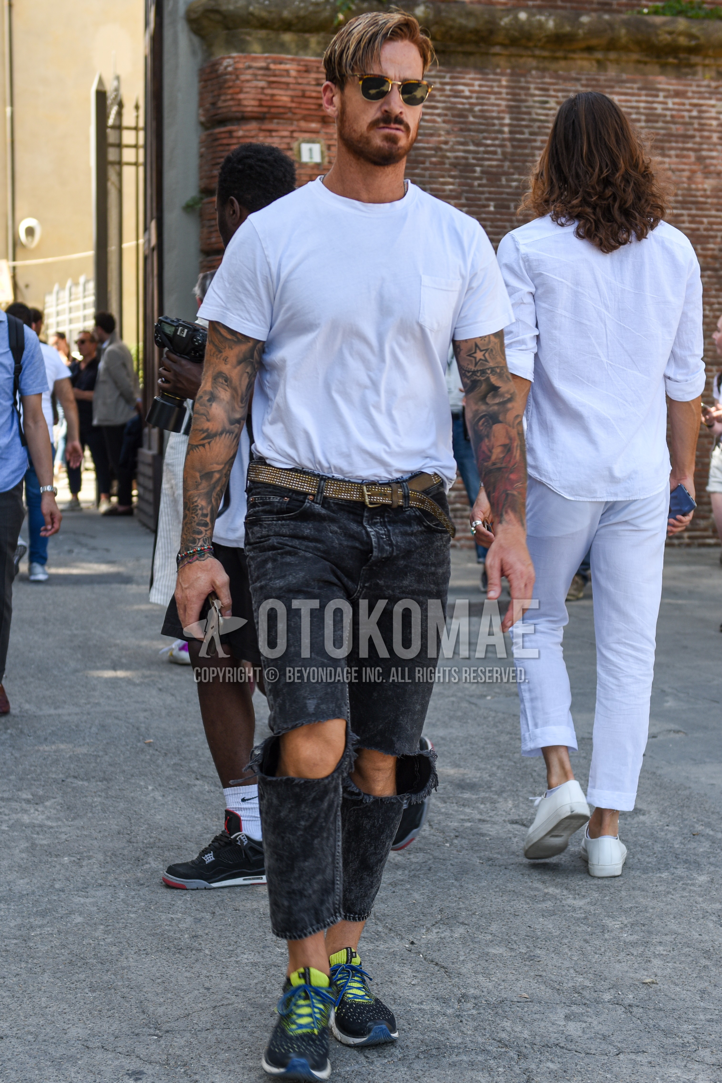 Men's summer outfit with black brown tortoiseshell sunglasses, white plain t-shirt, brown plain leather belt, dark gray plain damaged jeans, multi-color low-cut sneakers.