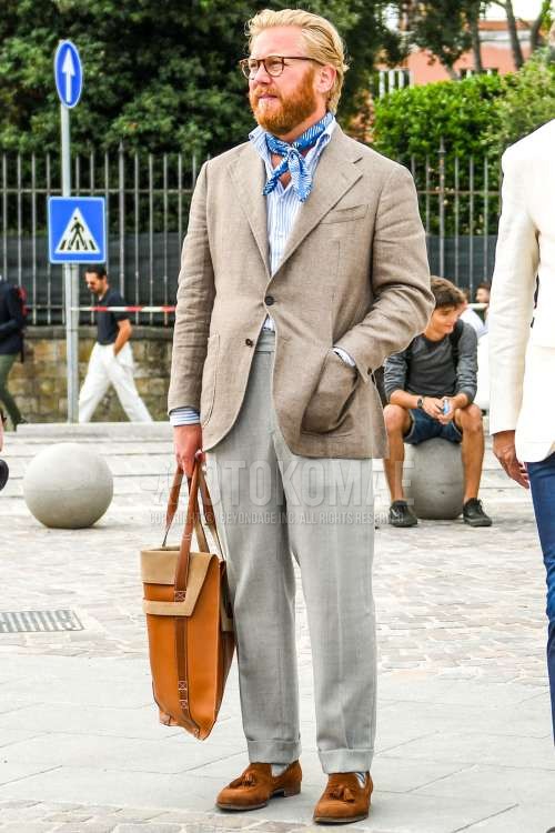 無地のメガネ、ブルーストールのバンダナ/ネッカチーフ、ベージュ無地のテーラードジャケット、白・ブルーストライプのシャツ、グレー無地のベルトレスパンツ、無地のスラックス、グレー無地のソックス、スエードのブラウンタッセルローファーの革靴、ベージュ無地のブリーフケース/ハンドバッグを合わせた春夏秋のメンズコーデ・着こなし。