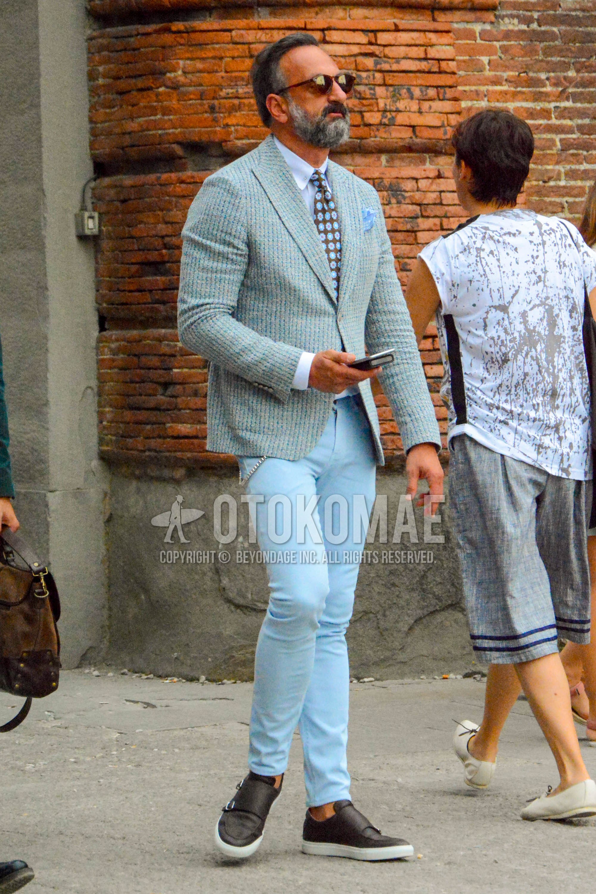 Men's spring summer autumn outfit with plain sunglasses, light blue outerwear tailored jacket, white plain shirt, light blue plain cotton pants, brown slip-on sneakers, brown dots necktie.