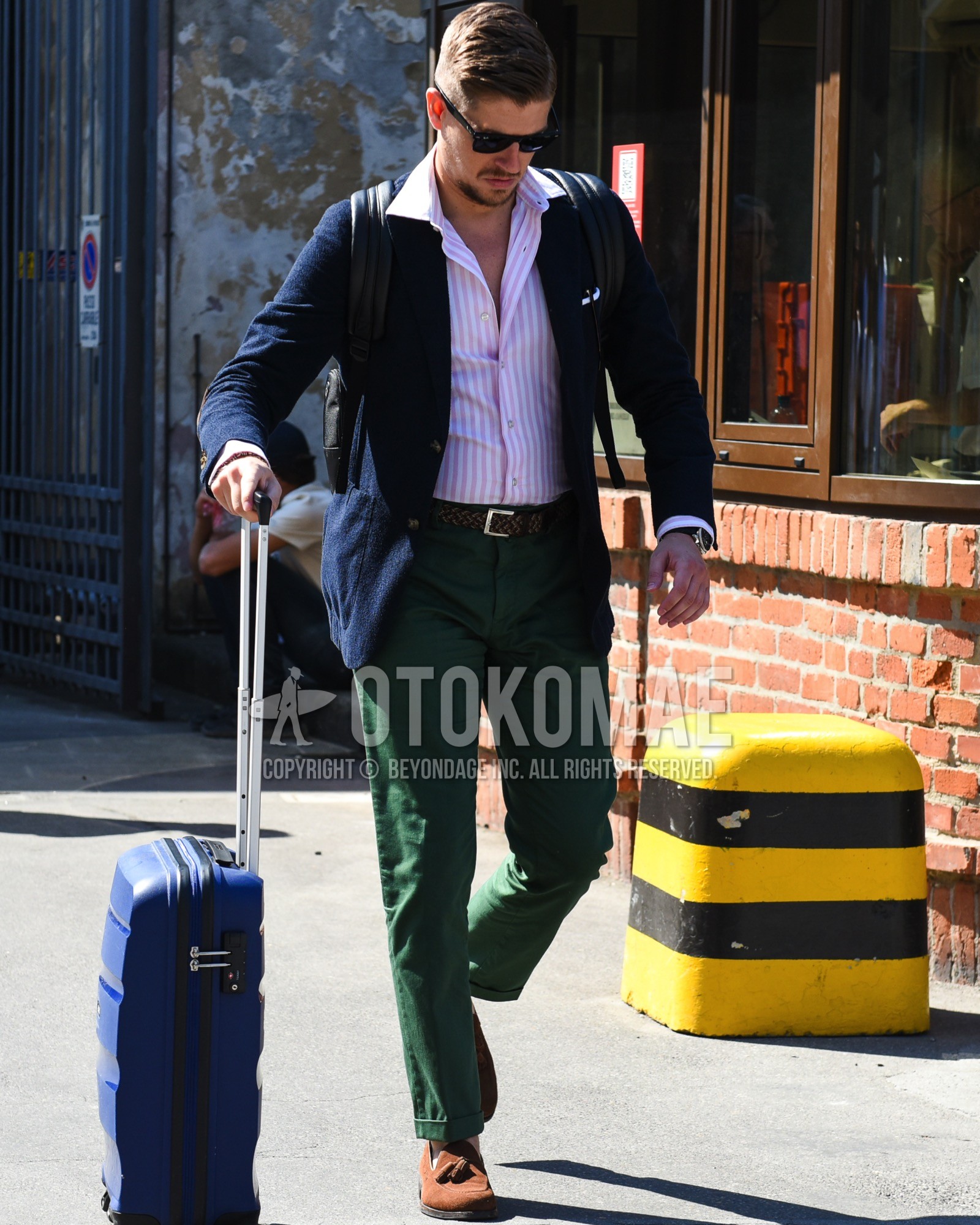 Men's spring summer outfit with black plain sunglasses, navy plain tailored jacket, pink white stripes shirt, brown plain braided belt, green leopard chinos, brown tassel loafers leather shoes, brown suede shoes leather shoes, black plain backpack, black plain backpack.