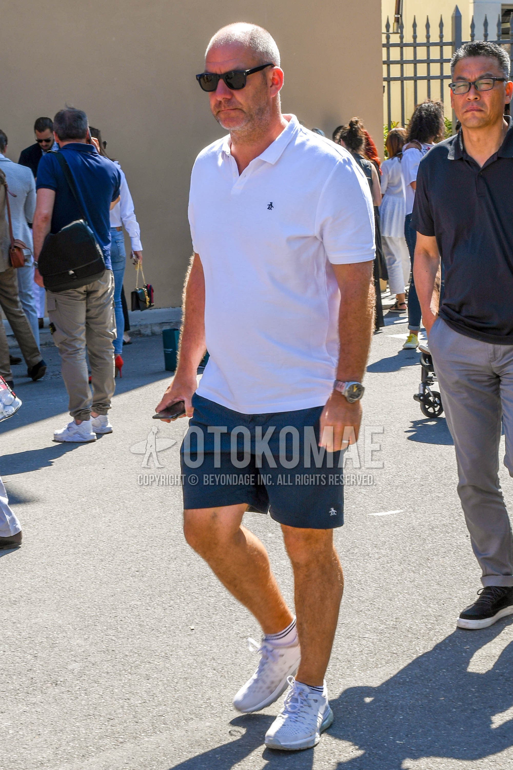 Men's summer outfit with plain sunglasses, white one point polo shirt, navy plain short pants, white stripes socks, white low-cut sneakers.