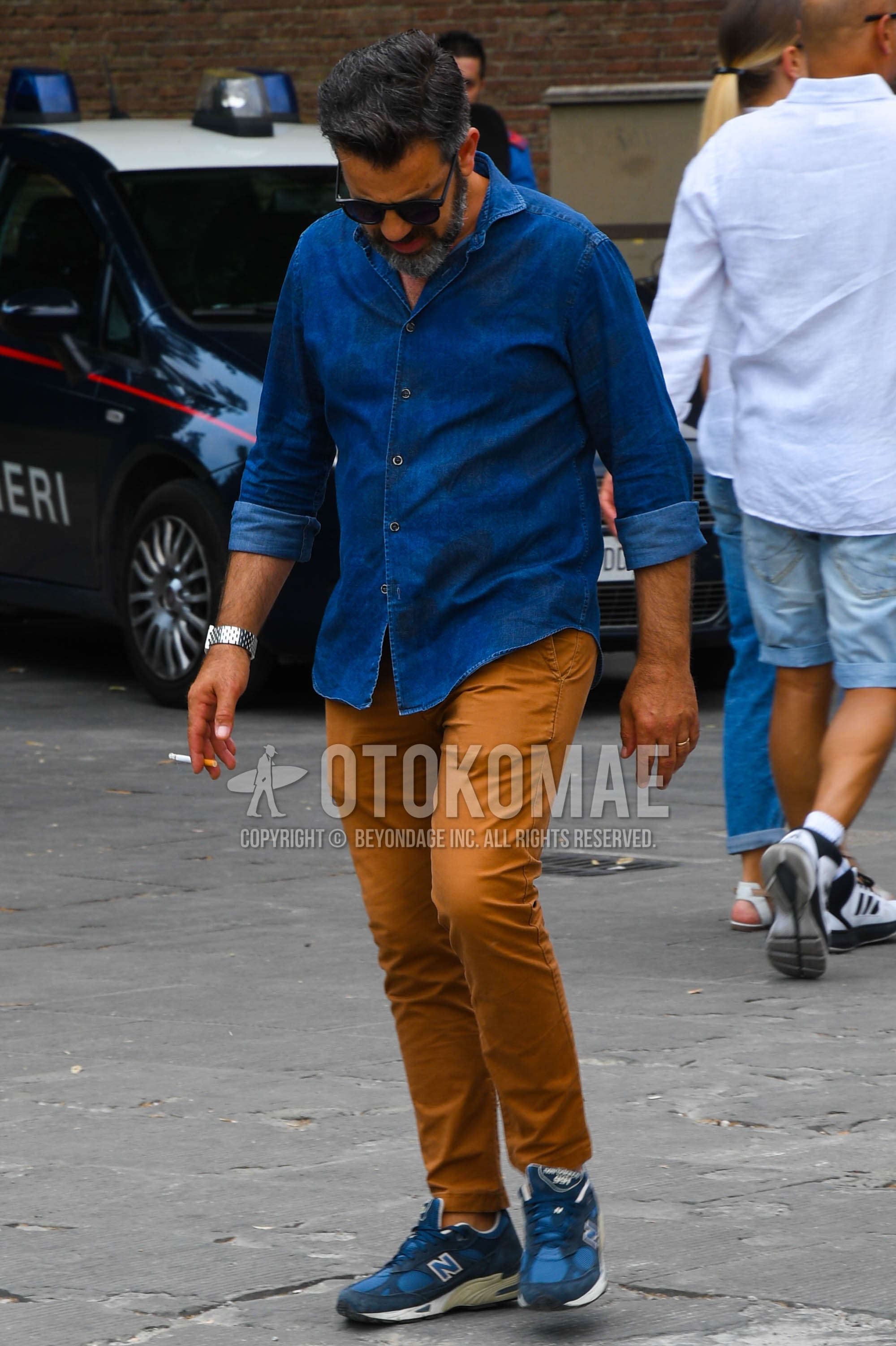 Men's spring summer outfit with plain sunglasses, blue plain denim shirt/chambray shirt, beige plain chinos, navy low-cut sneakers.
