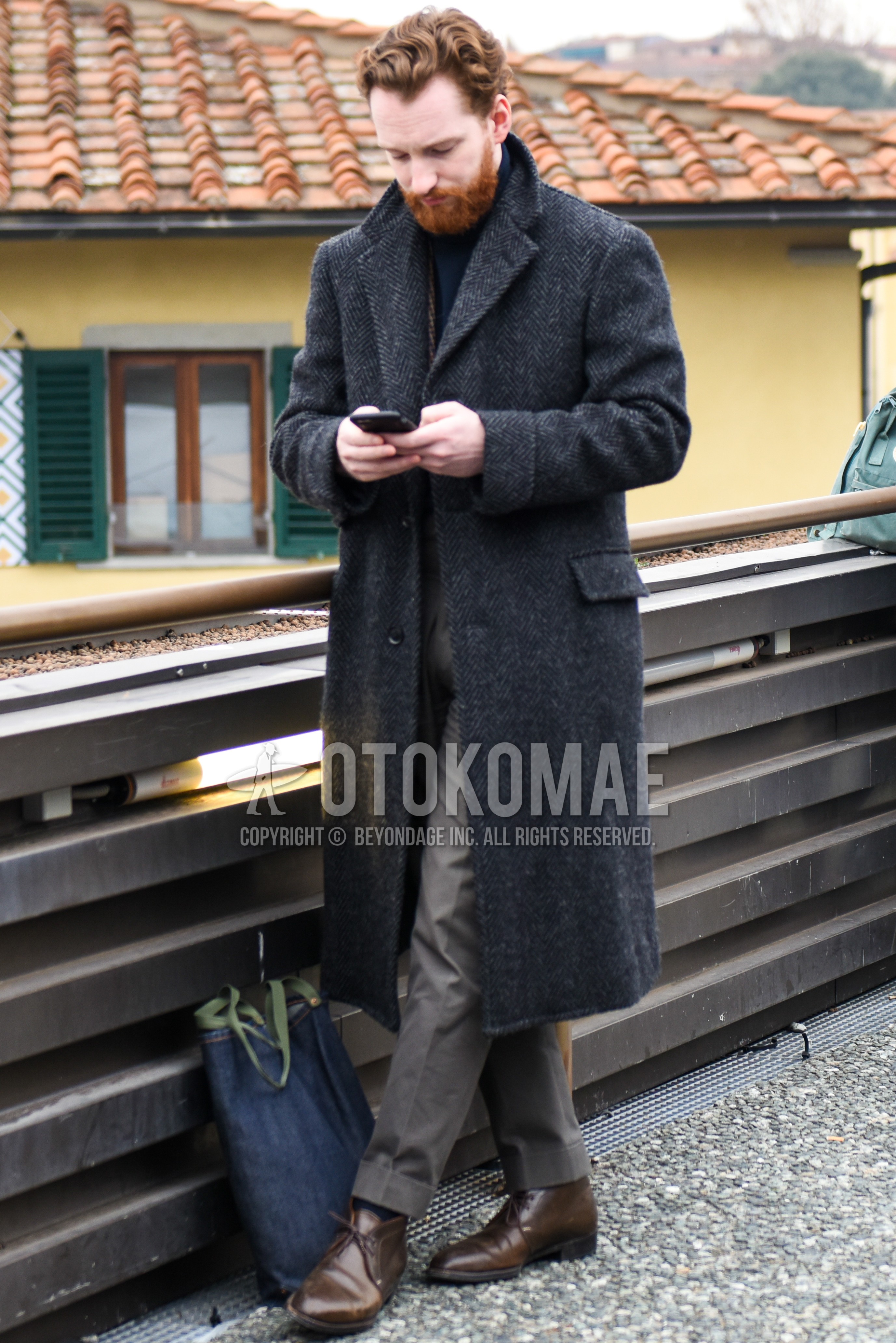 Men's winter outfit with dark gray plain chester coat, gray plain slacks, brown chukka boots, navy plain tote bag.