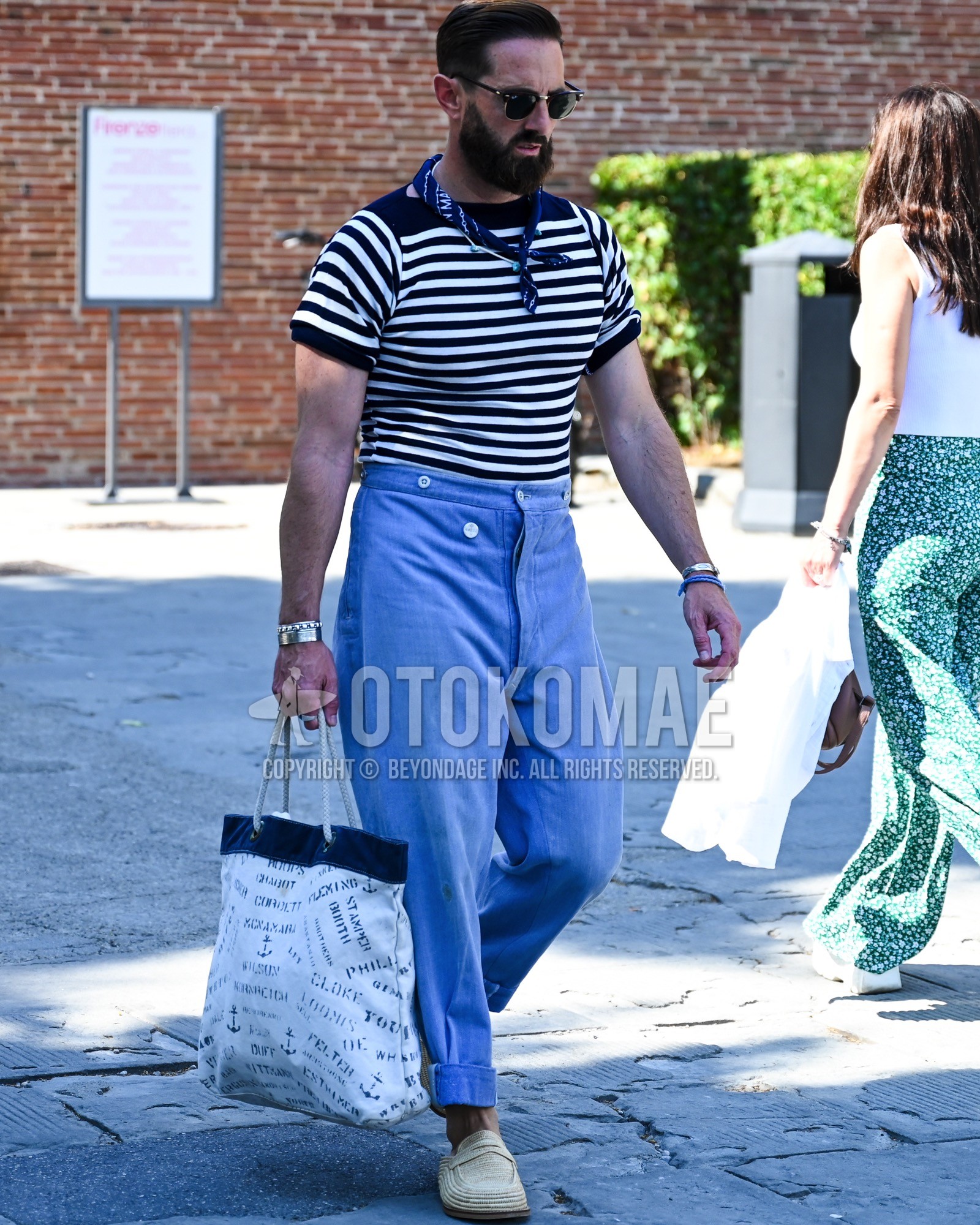 Men's spring summer outfit with black plain sunglasses, navy whole pattern bandana/neckerchief, white navy horizontal stripes t-shirt, light blue plain bottoms, beige coin loafers leather shoes, white whole pattern tote bag.