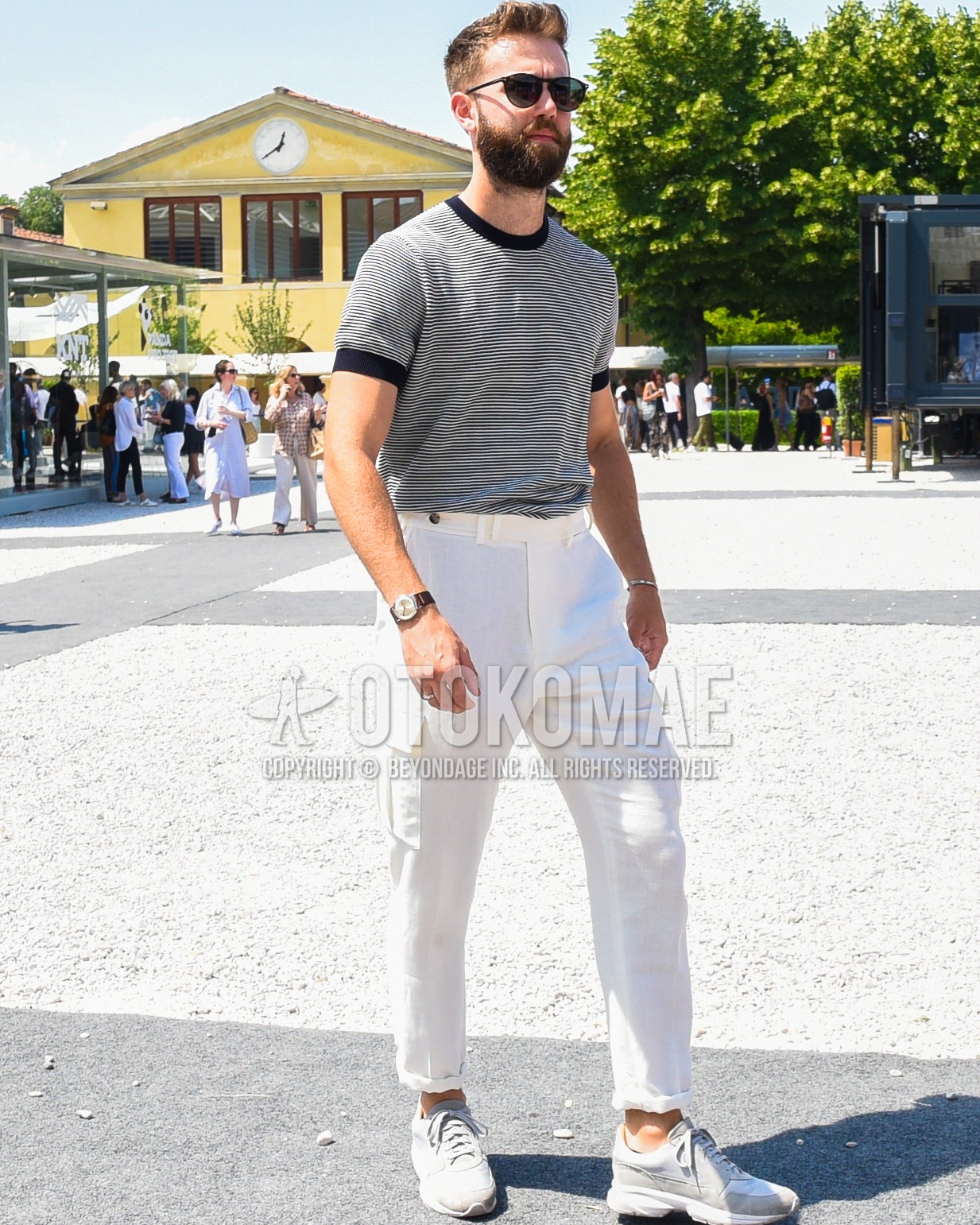 Men's spring summer outfit with black plain sunglasses, black horizontal stripes t-shirt, white plain cargo pants, gray low-cut sneakers.