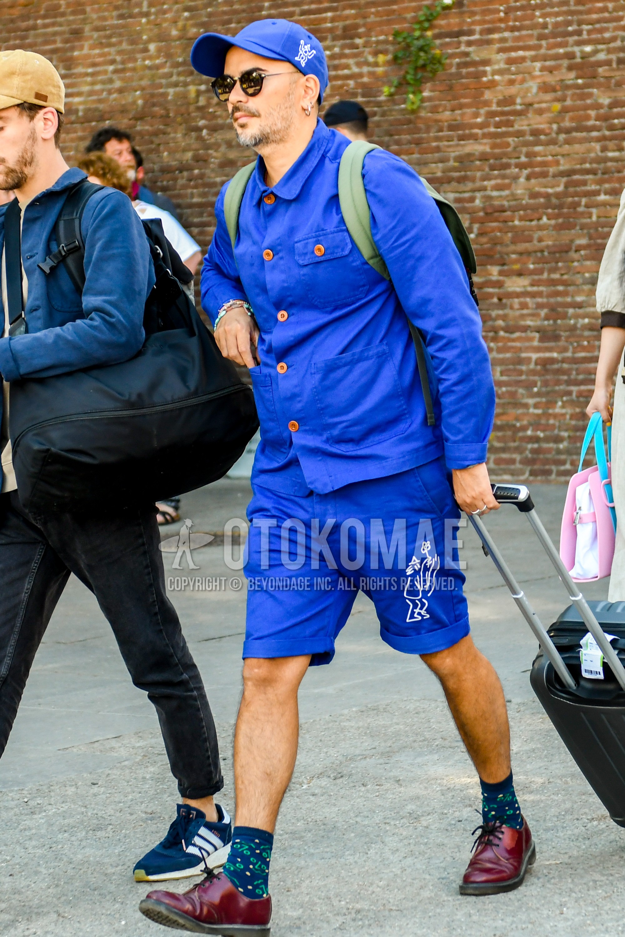 Men's spring summer autumn outfit with blue plain baseball cap, plain sunglasses, blue plain shirt jacket, blue plain short pants, navy botanical socks, red straight-tip shoes leather shoes.