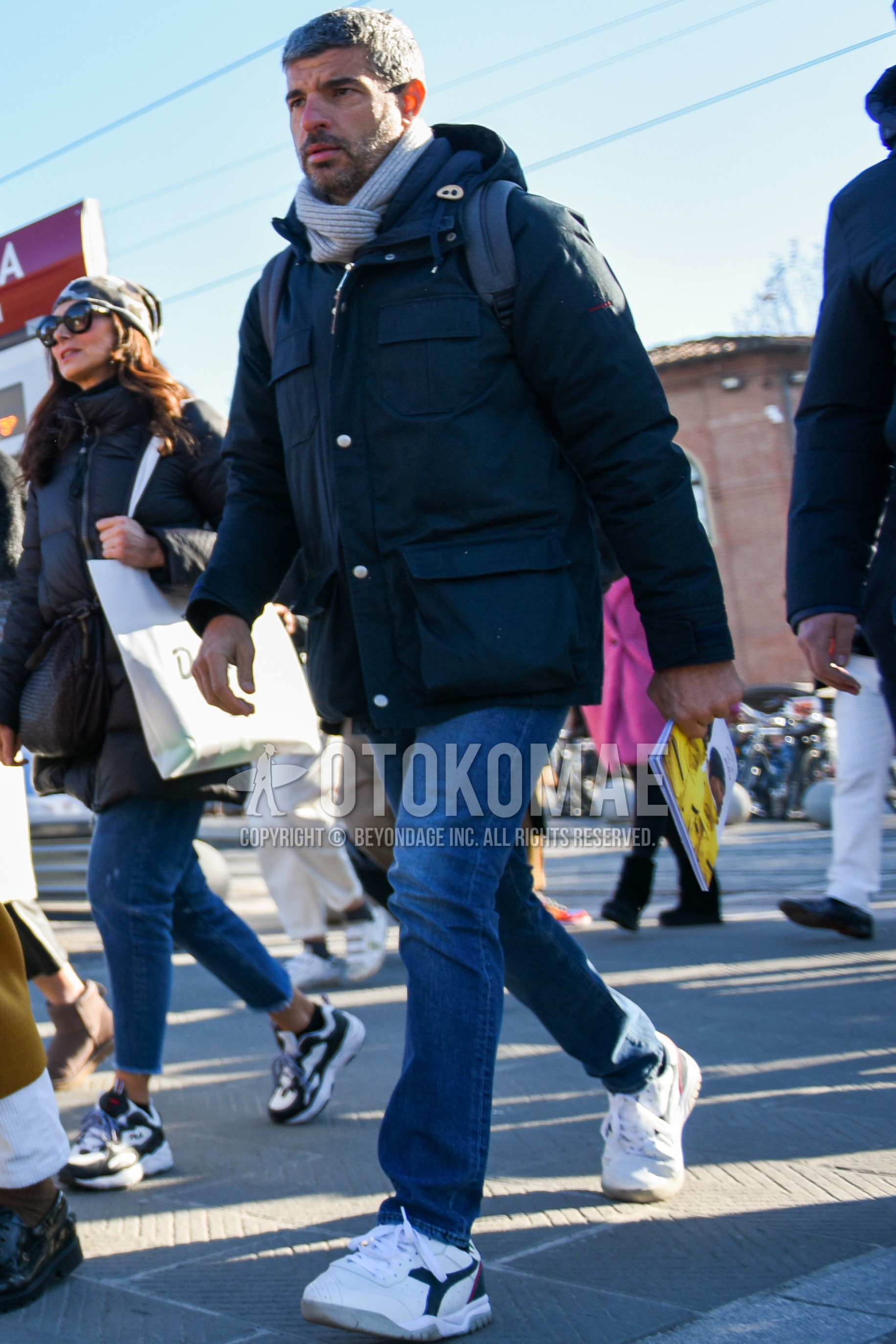 Men's winter outfit with gray plain scarf, navy plain down jacket, blue plain denim/jeans, white low-cut sneakers.