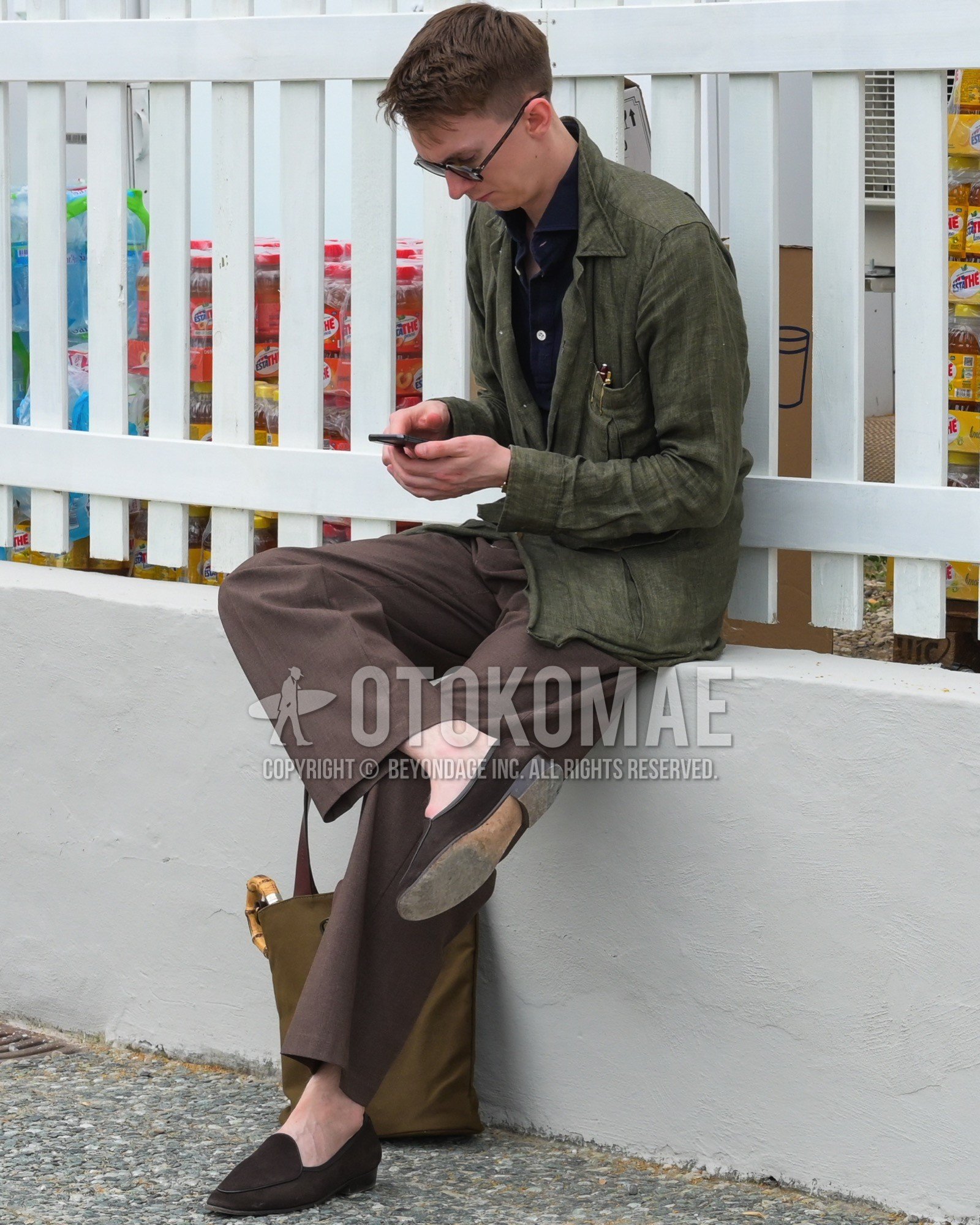 Men's spring summer autumn outfit with black plain sunglasses, olive green plain coverall, navy plain shirt, brown plain slacks, brown  loafers leather shoes, brown suede shoes leather shoes, brown plain tote bag.