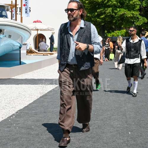 黒無地のサングラス、黒無地のカジュアルベスト、グレー無地のシャツ、ブラウン無地のレザーベルト、ブラウン無地のスラックス、ブラウン無地のプリーツパンツ、ブラウンローファーの革靴を合わせた夏春のメンズコーデ・着こなし。