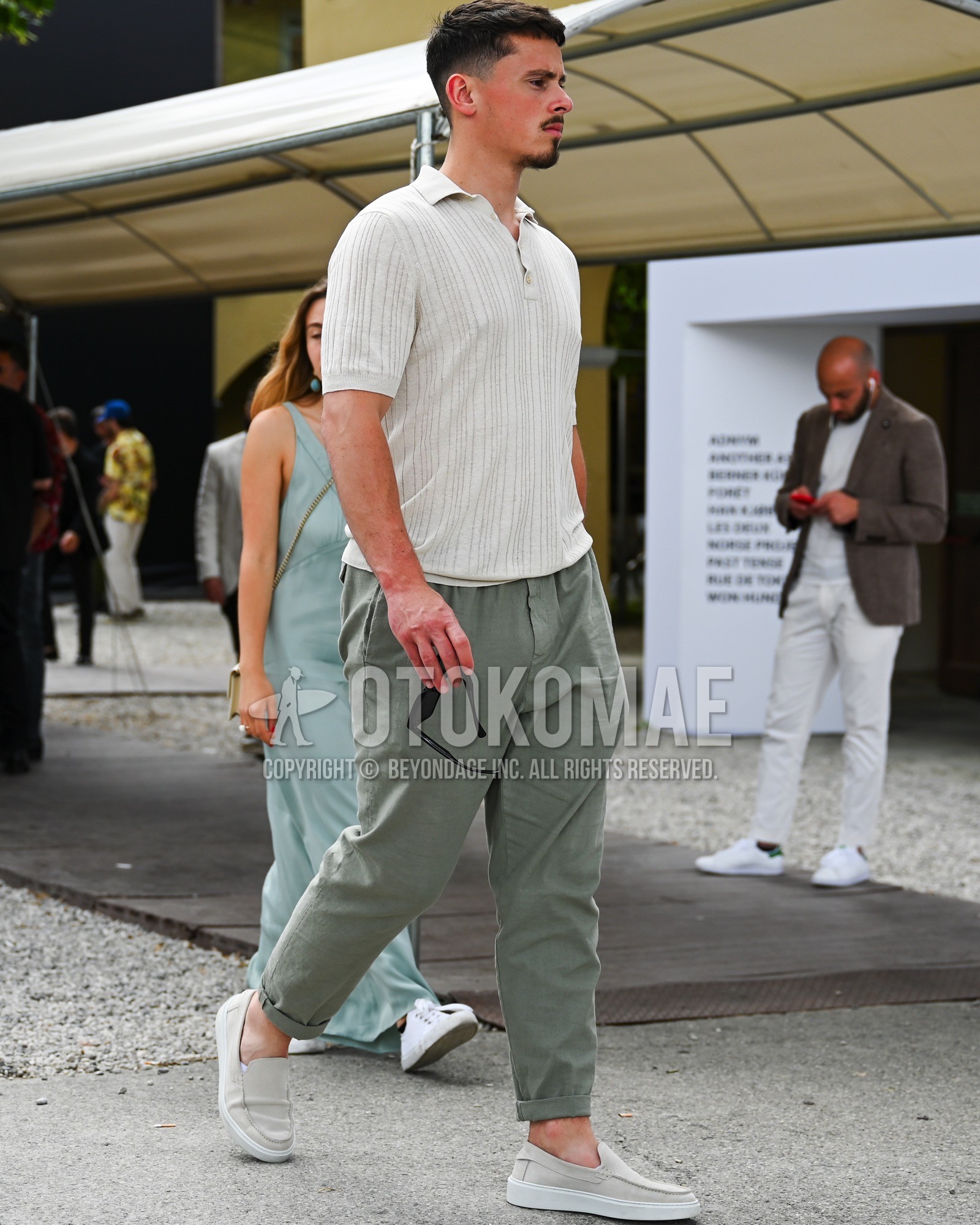 Men's spring summer outfit with beige stripes polo shirt, green plain slacks, gray slip-on sneakers.