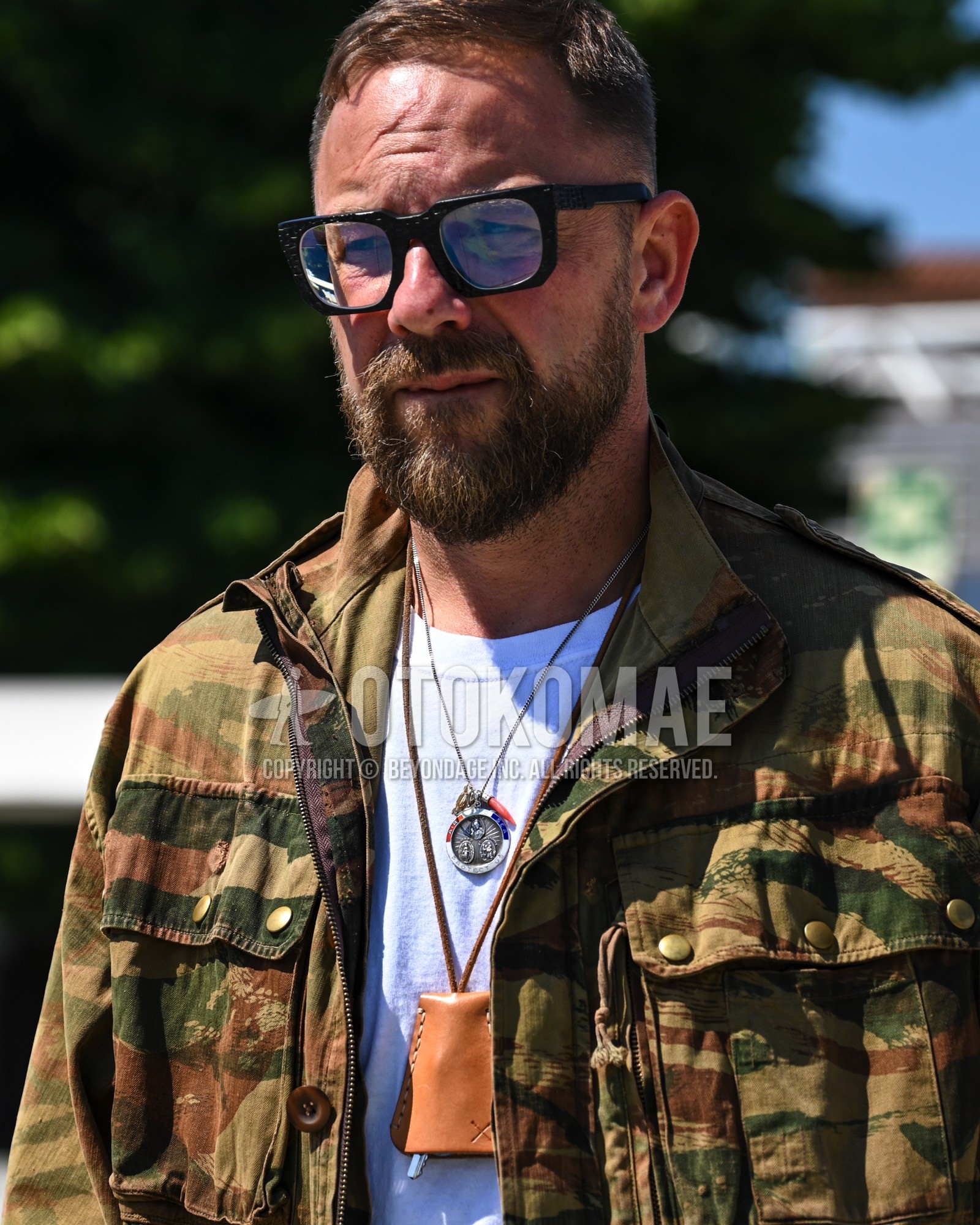 Men's spring summer autumn outfit with clear plain sunglasses, beige camouflage military jacket, white plain t-shirt.