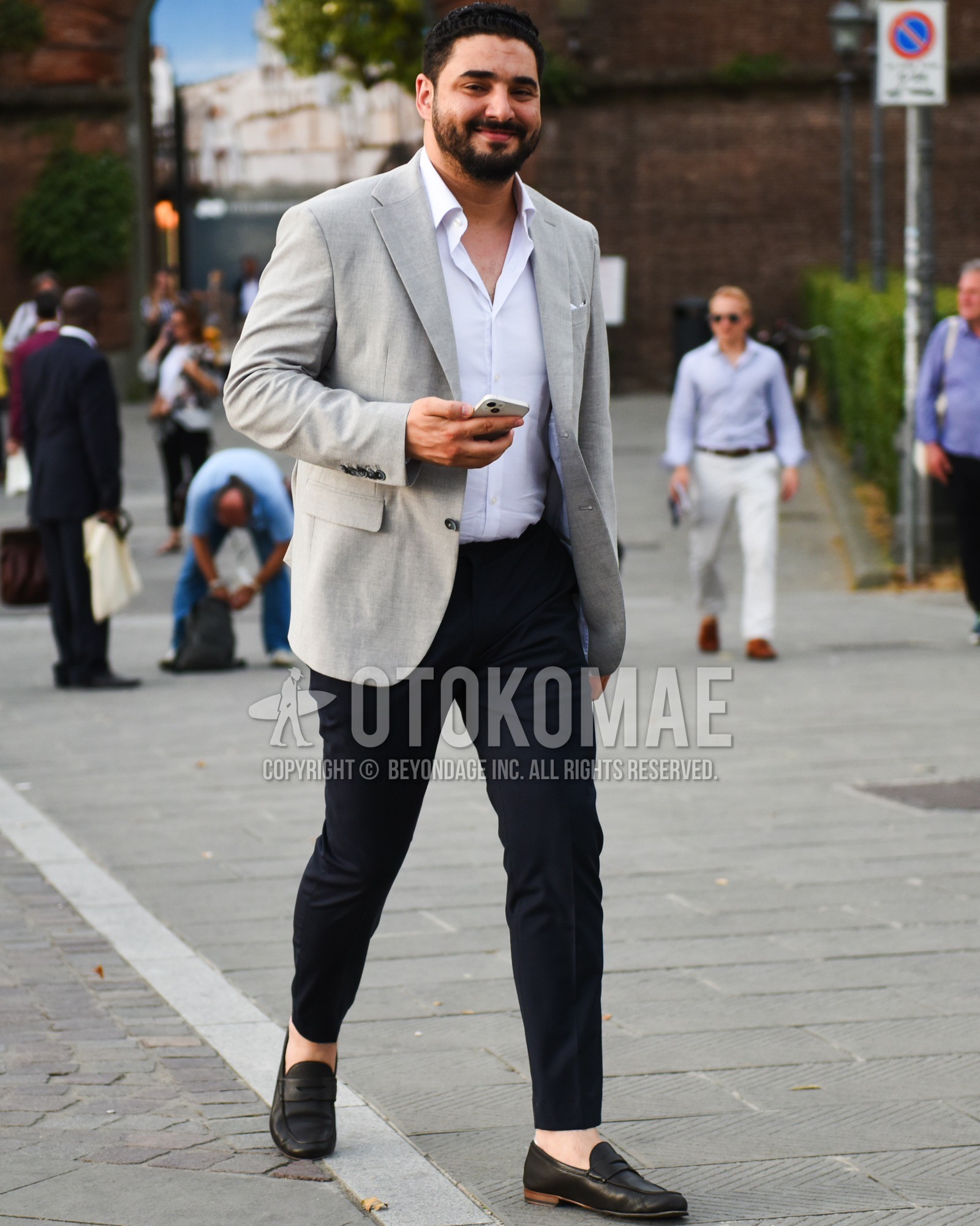 Men's spring summer outfit with gray plain tailored jacket, white plain shirt, navy plain slacks, brown coin loafers leather shoes.
