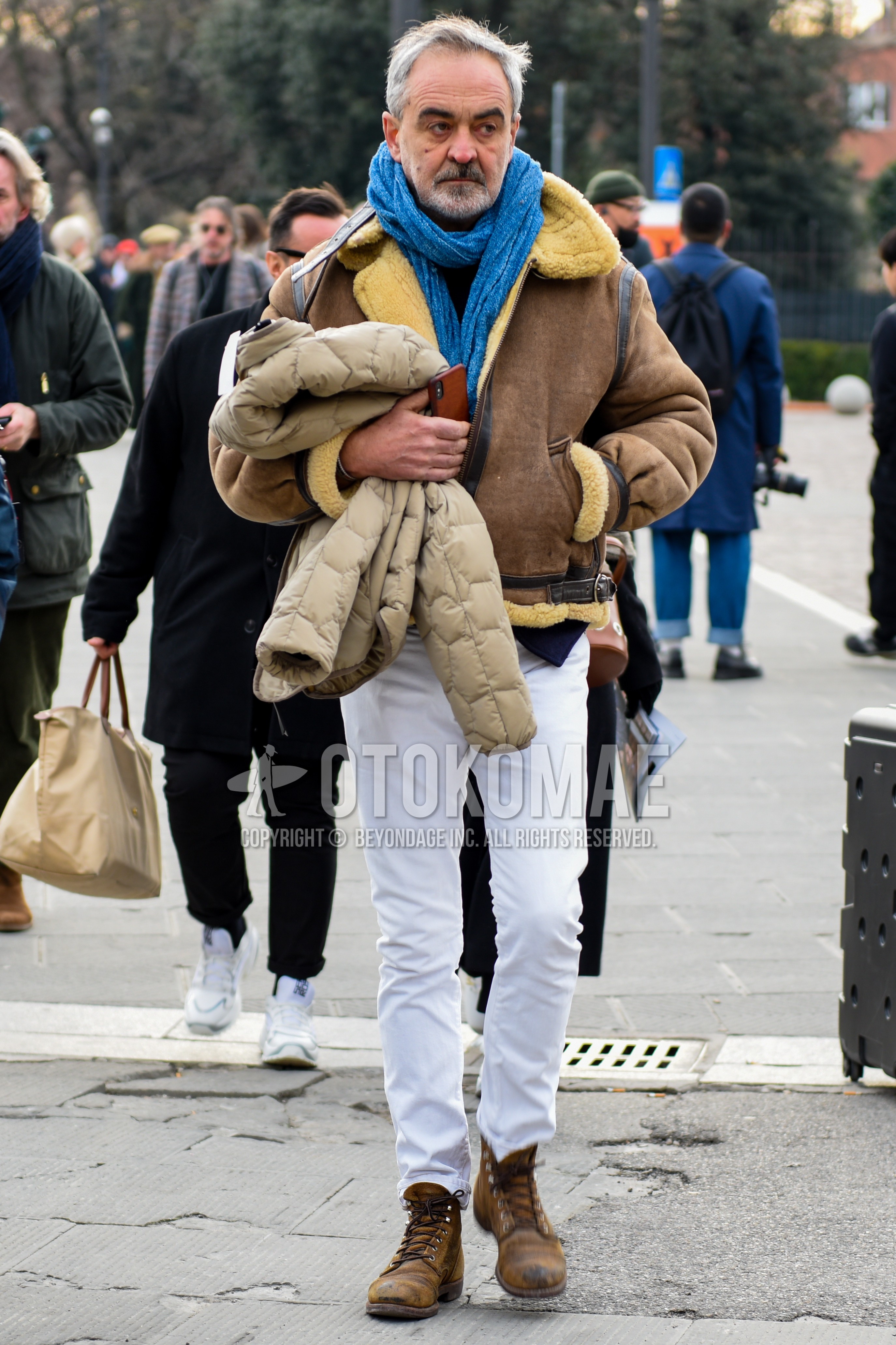 Men's autumn winter outfit with blue plain scarf, brown plain leather jacket, brown plain military jacket, white plain cotton pants, brown  boots.