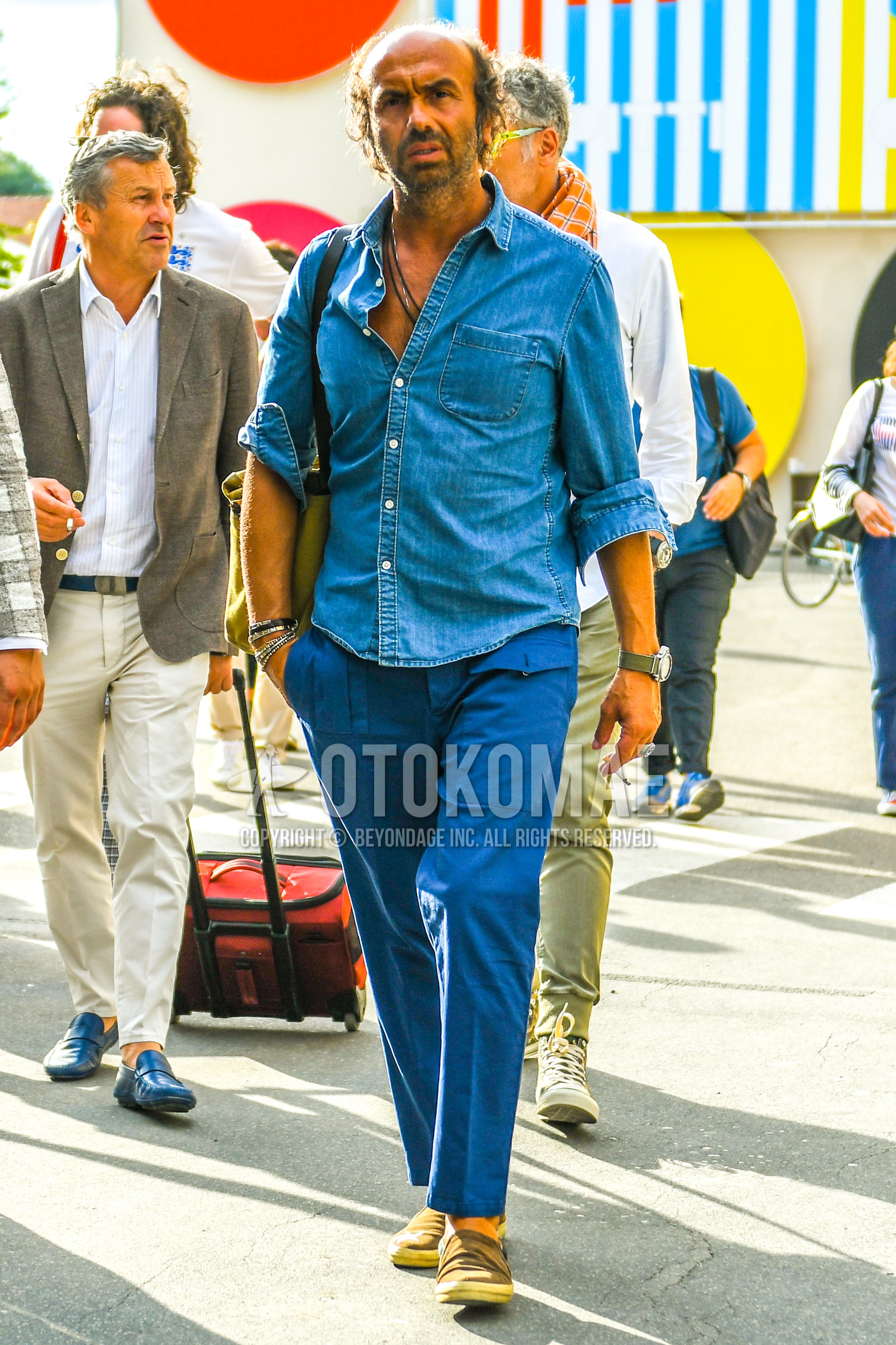 Men's spring summer outfit with blue plain denim shirt/chambray shirt, blue plain cargo pants, beige slip-on sneakers.