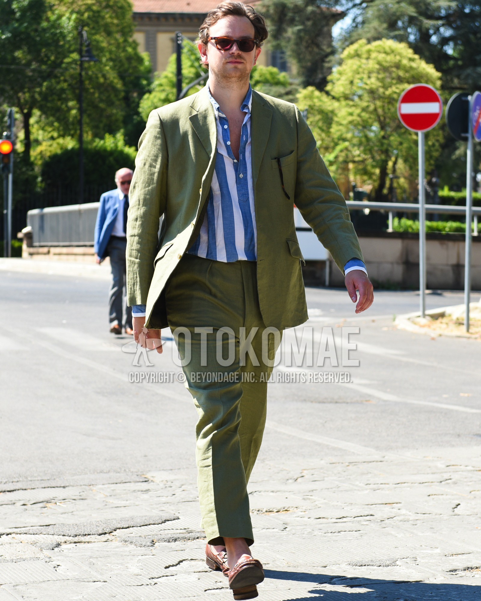 Men's spring summer outfit with brown tortoiseshell sunglasses, blue white stripes shirt, brown u-tip shoes leather shoes, olive green plain suit.