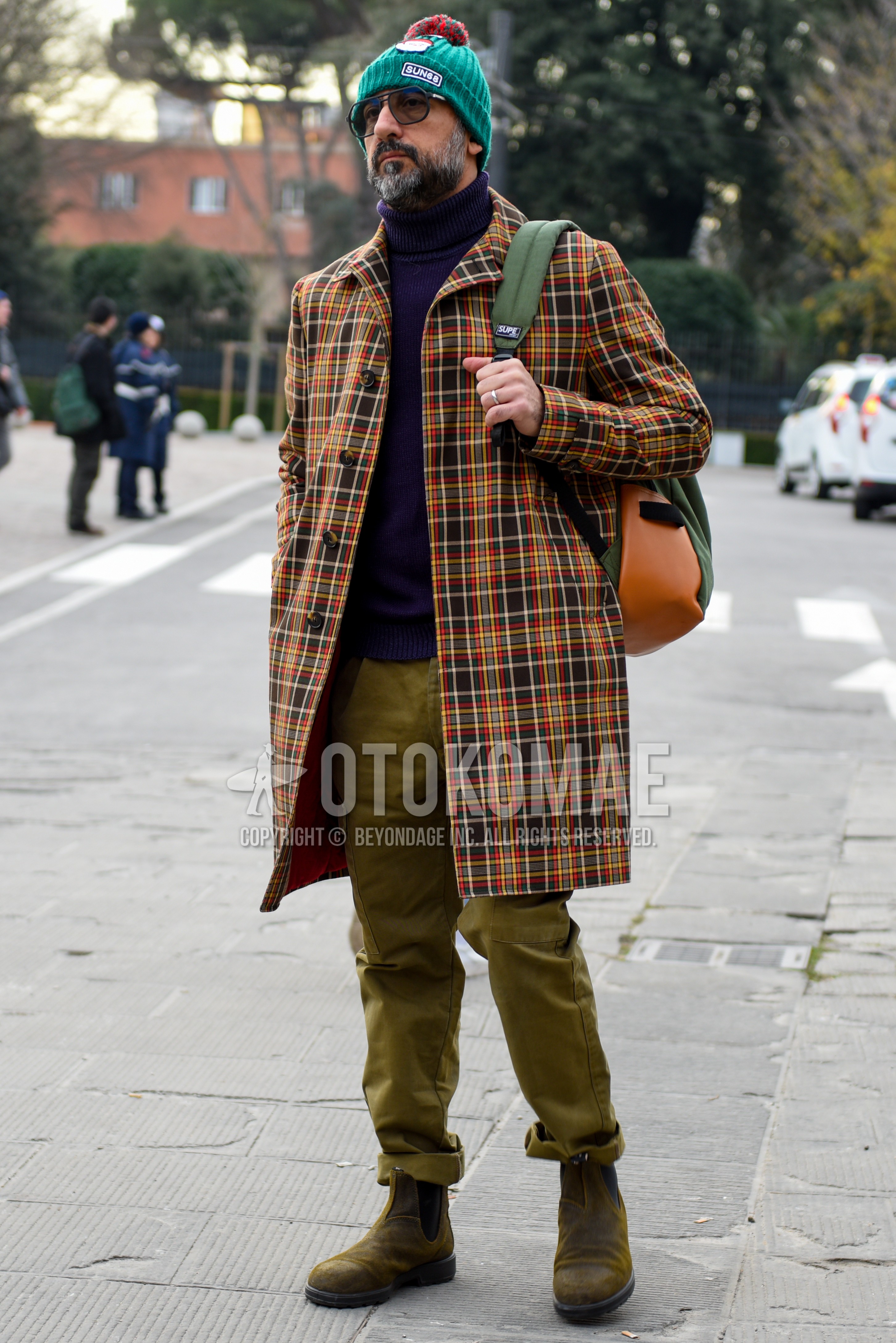 Men's autumn winter outfit with green plain knit cap, multi-color check stenkarrer coat, purple plain turtleneck knit, beige plain chinos, beige side-gore boots, green plain backpack.
