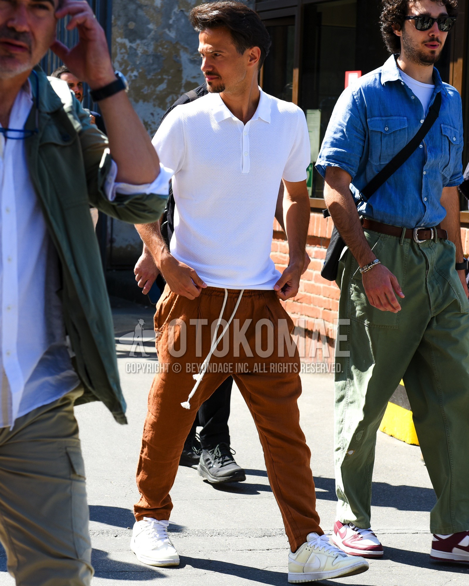 Men's spring summer outfit with white plain polo shirt, brown plain easy pants, white beige low-cut sneakers.