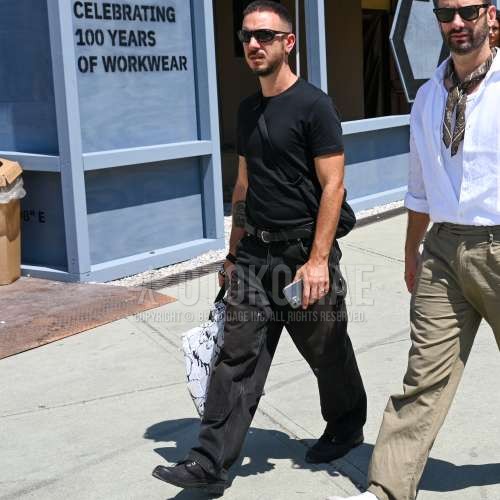 黒無地のサングラス、黒無地のTシャツ、黒無地のレザーベルト、黒無地のデニム/ジーンズ、黒モカシン/デッキシューズの革靴、黒無地のショルダーバッグ、白バッグのトートバッグを合わせた夏春のメンズコーデ・着こなし。