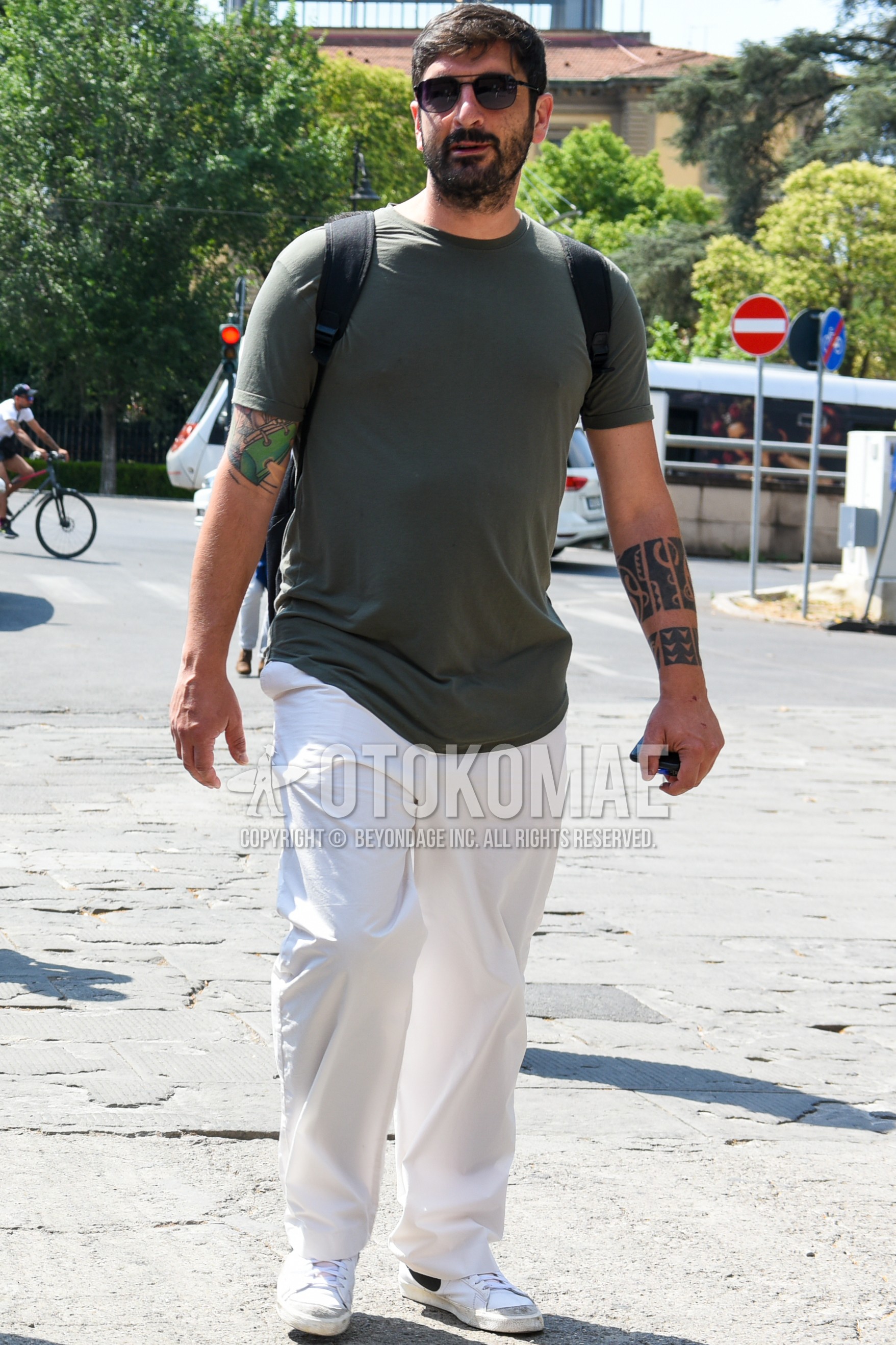 Men's summer outfit with black plain sunglasses, olive green plain t-shirt, white plain wide pants, white low-cut sneakers, black plain backpack.