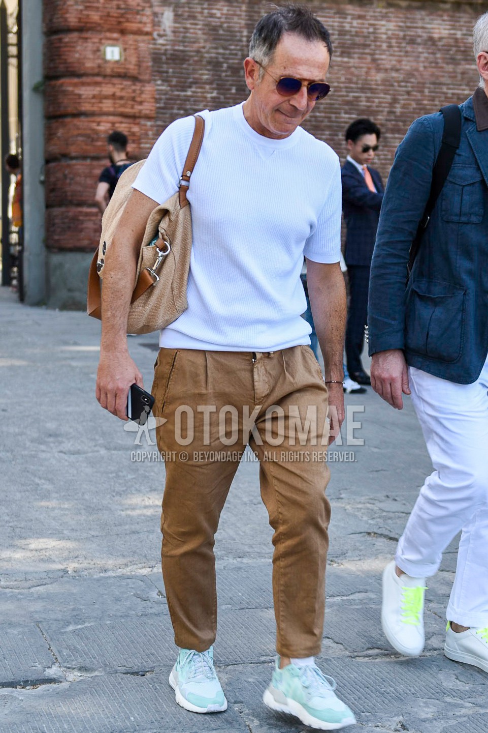 Men's summer outfit with gold brown plain sunglasses, white plain t-shirt, brown plain ankle pants, light blue low-cut sneakers, brown plain bag.