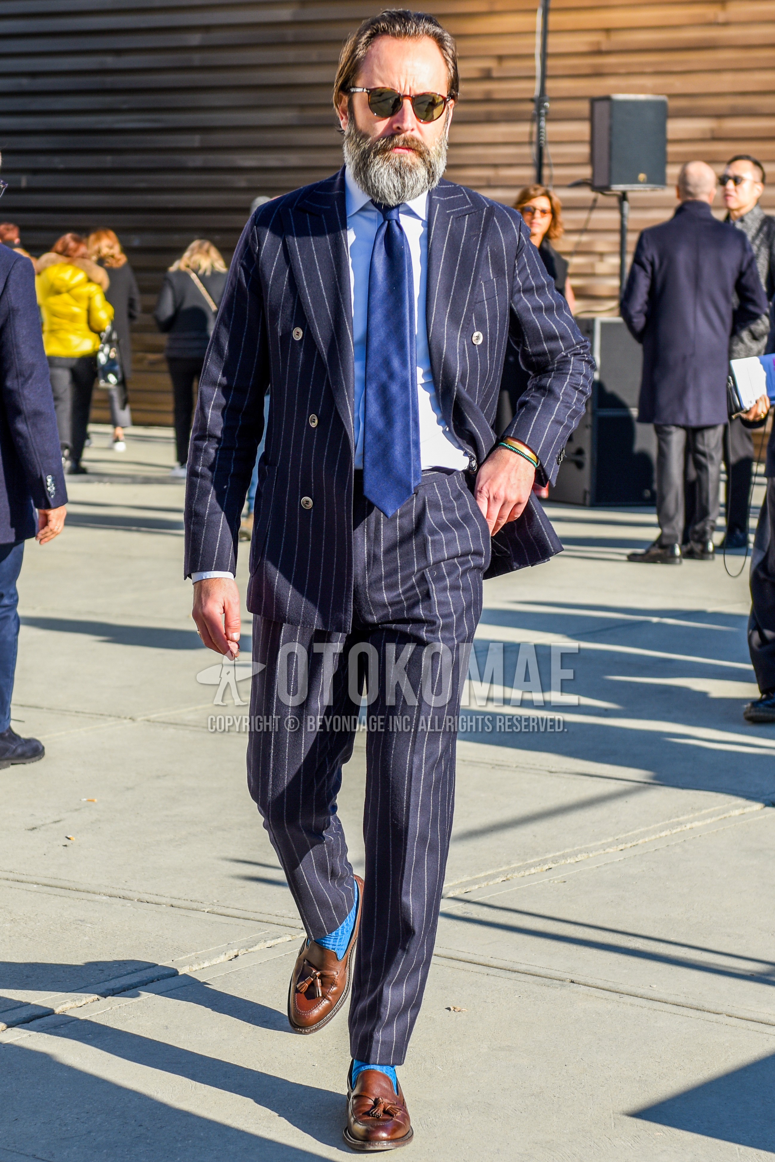 Men's spring autumn outfit with brown tortoiseshell sunglasses, white plain shirt, blue plain socks, navy stripes suit, navy plain necktie.