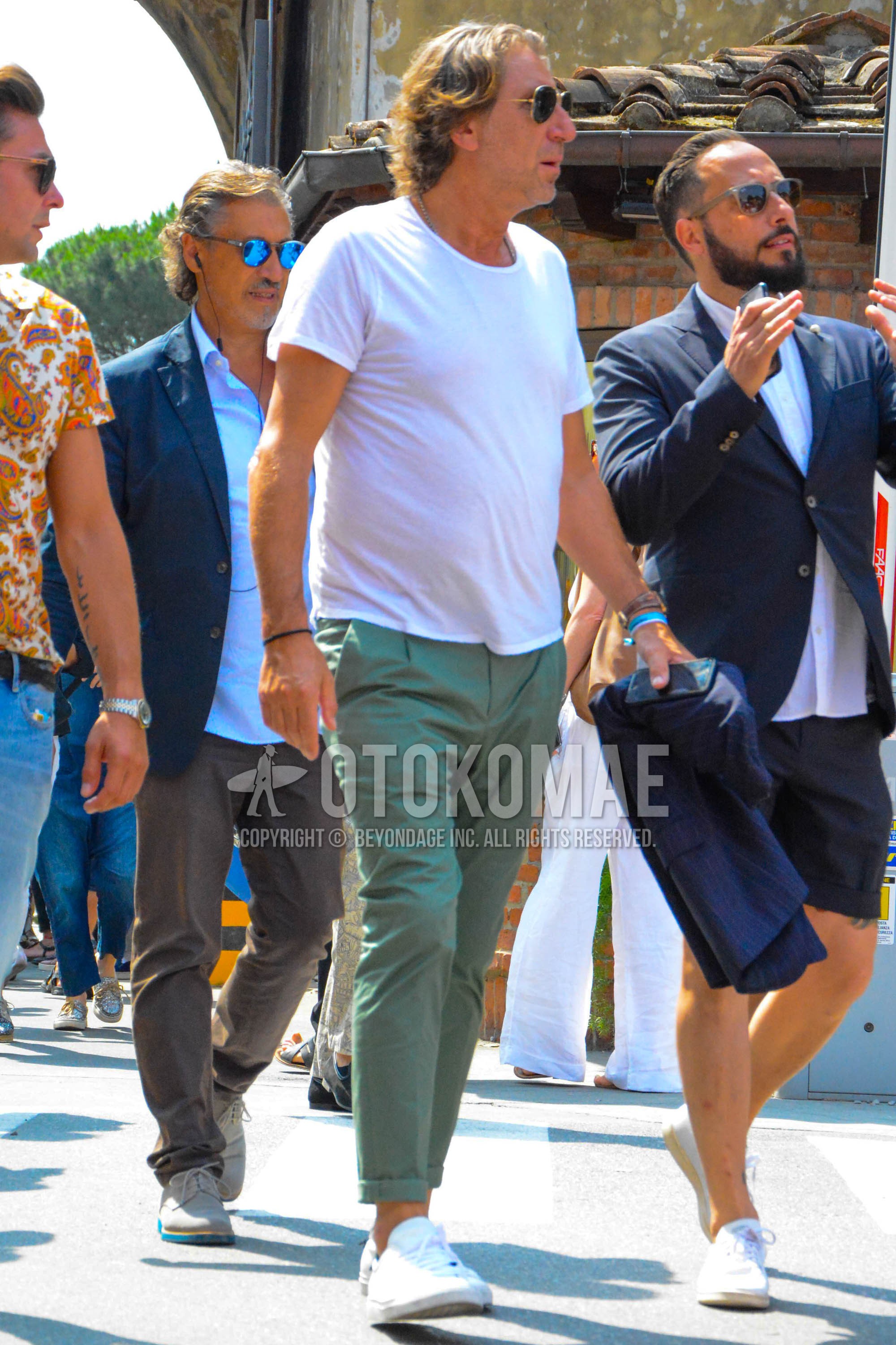 Men's spring summer outfit with gold plain sunglasses, white plain t-shirt, olive green plain chinos, white low-cut sneakers.