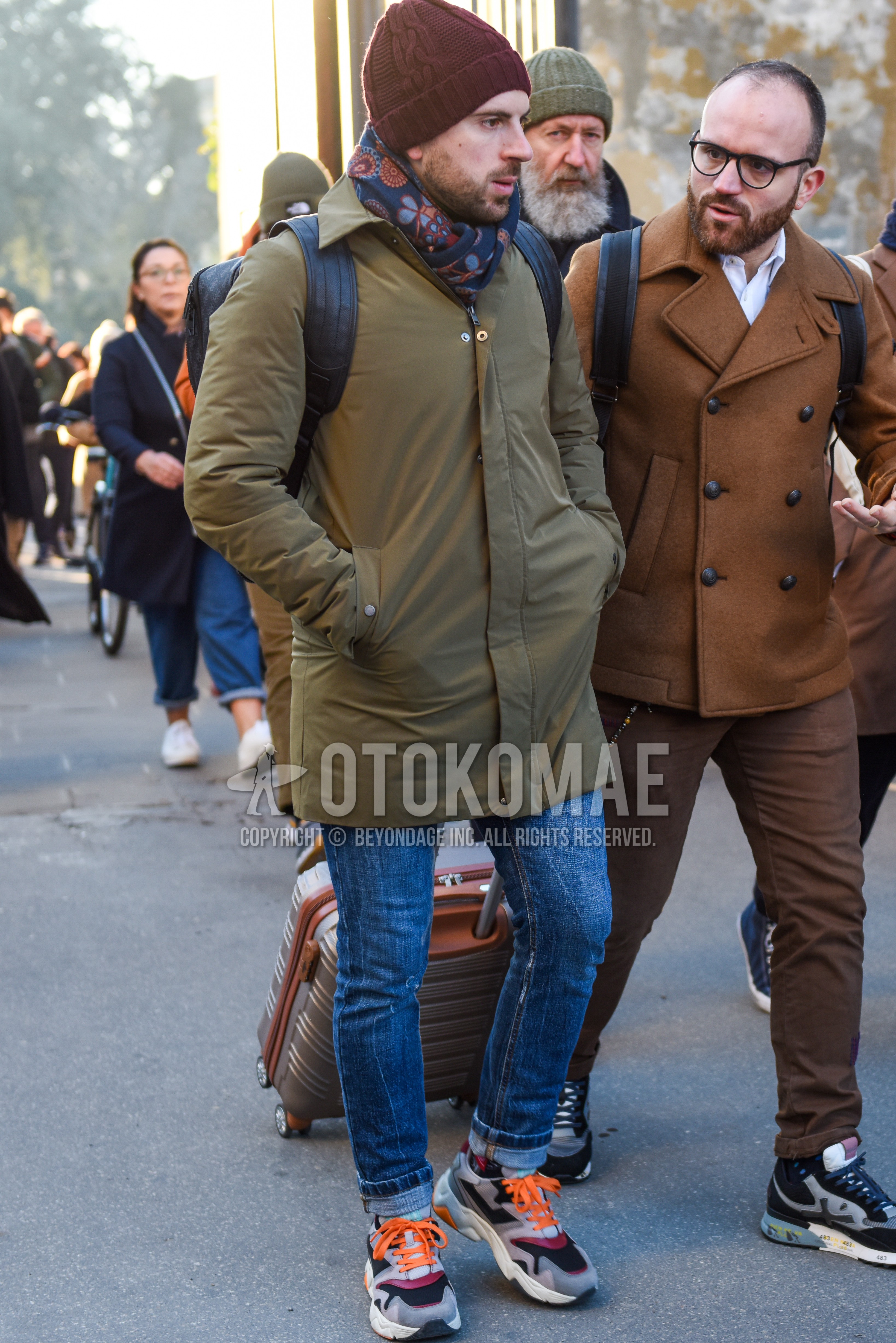 Men's autumn winter outfit with brown plain knit cap, multi-color scarf scarf, beige plain stenkarrer coat, blue plain denim/jeans, gray low-cut sneakers.