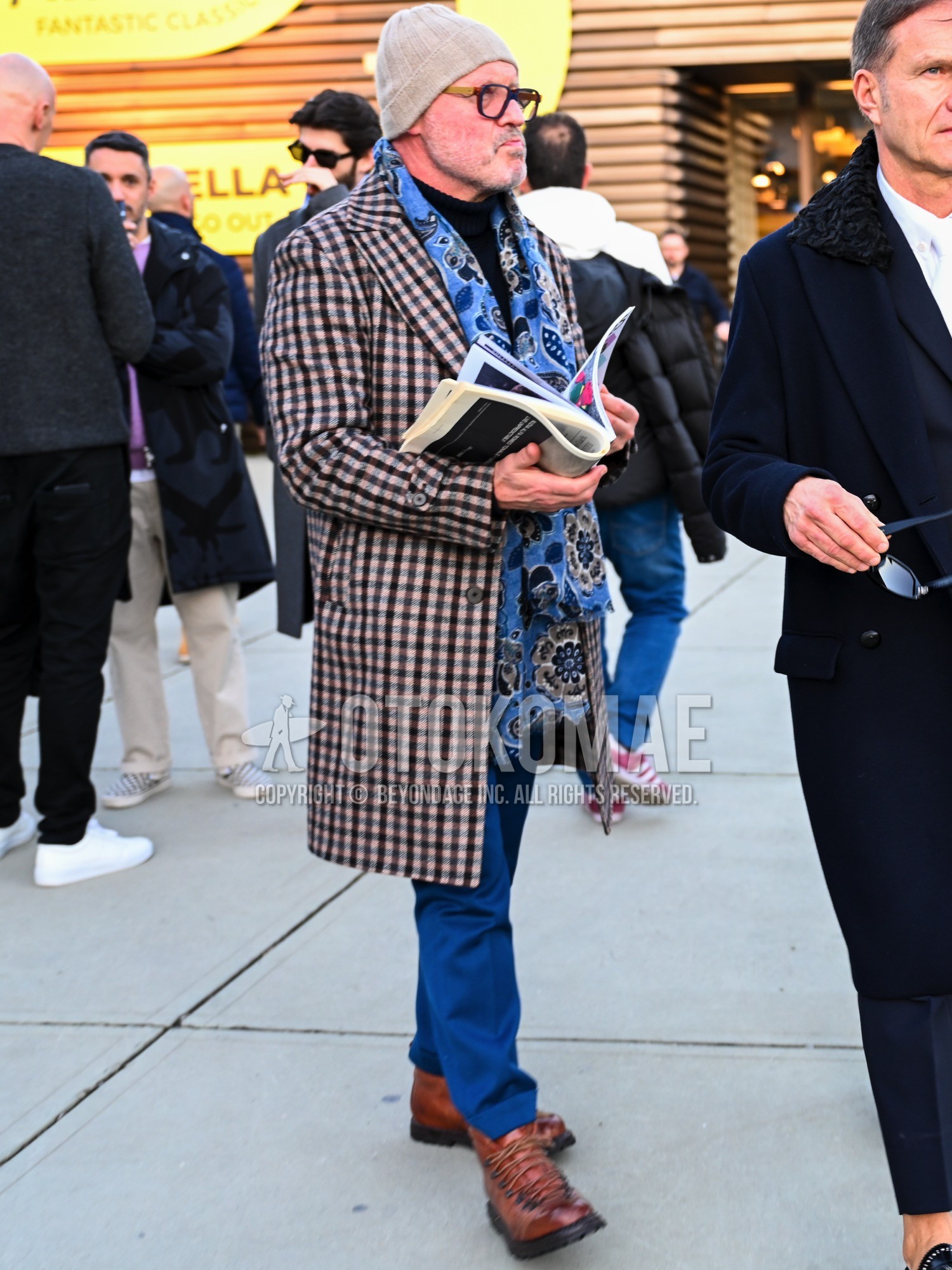Men's autumn winter outfit with beige plain knit cap, brown yellow plain glasses, blue graphic scarf, black plain t-shirt, blue plain slacks, brown work boots.