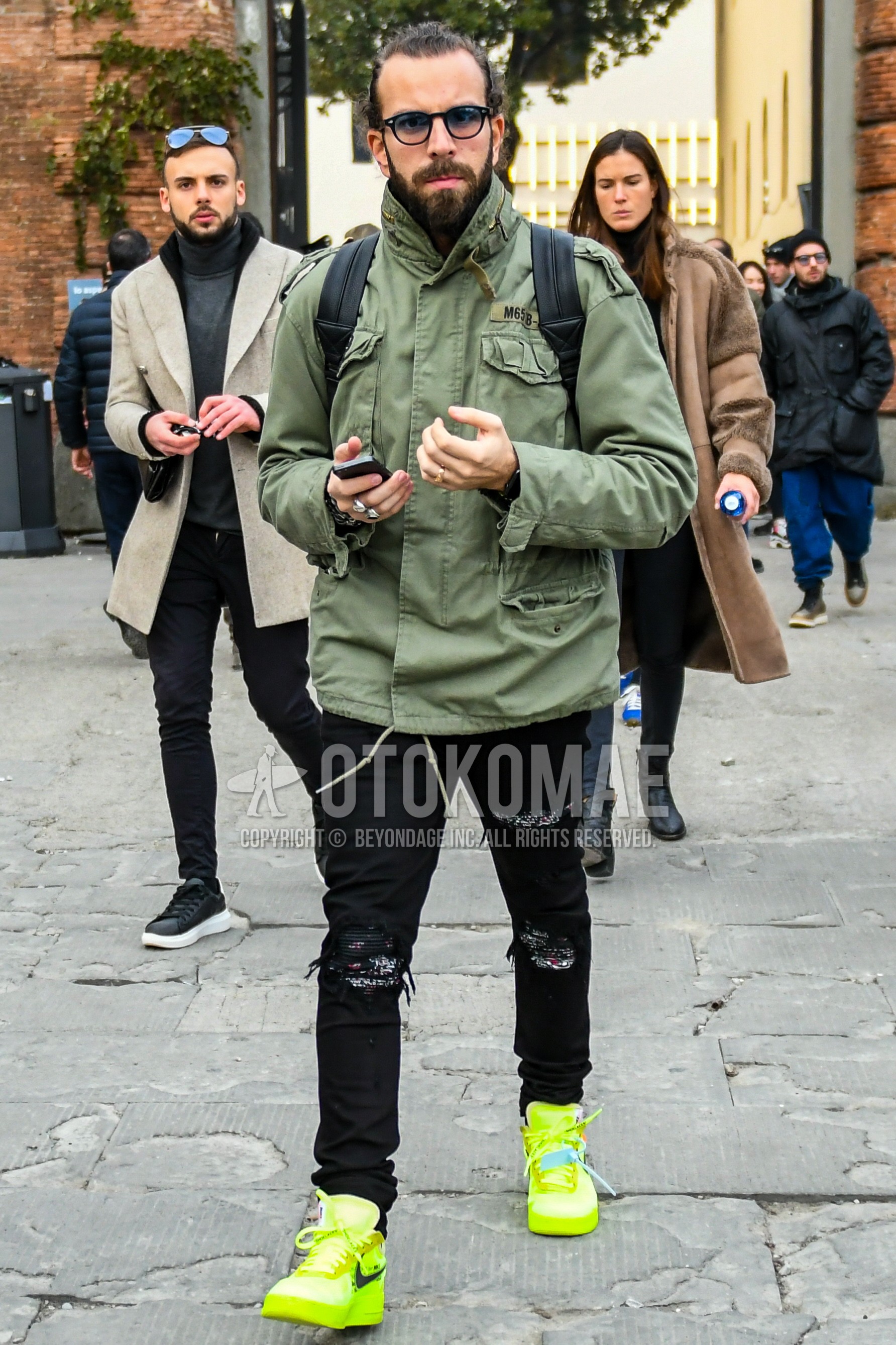 Men's spring autumn winter outfit with plain sunglasses, green plain M-65, black plain damaged jeans, yellow low-cut sneakers.