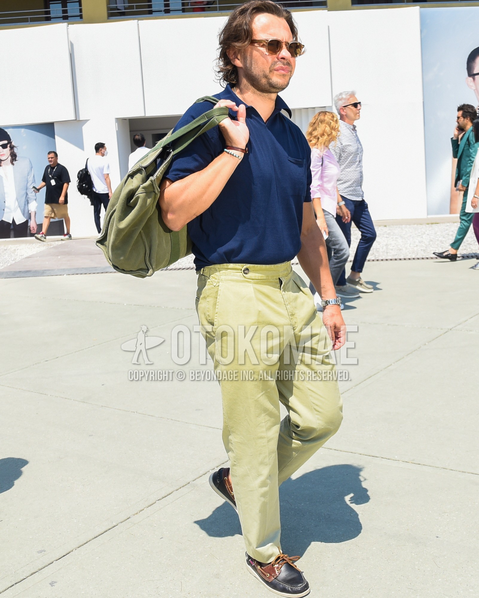 Men's spring summer outfit with brown plain sunglasses, navy plain t-shirt, beige plain chinos, black moccasins/deck shoes leather shoes, olive green plain tote bag.