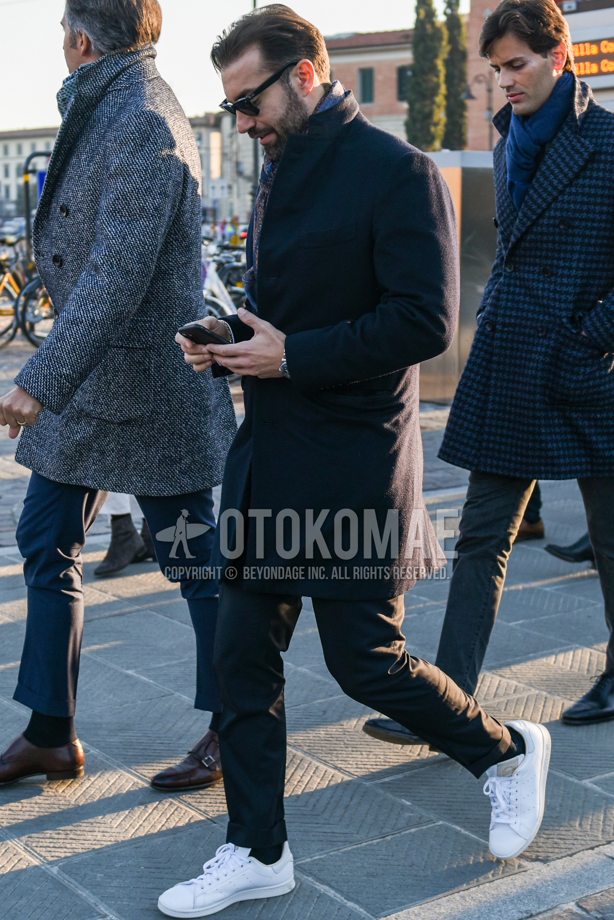 Men's autumn winter outfit with black plain sunglasses, multi-color scarf scarf, black plain chester coat, dark gray plain slacks, black plain socks, white low-cut sneakers.
