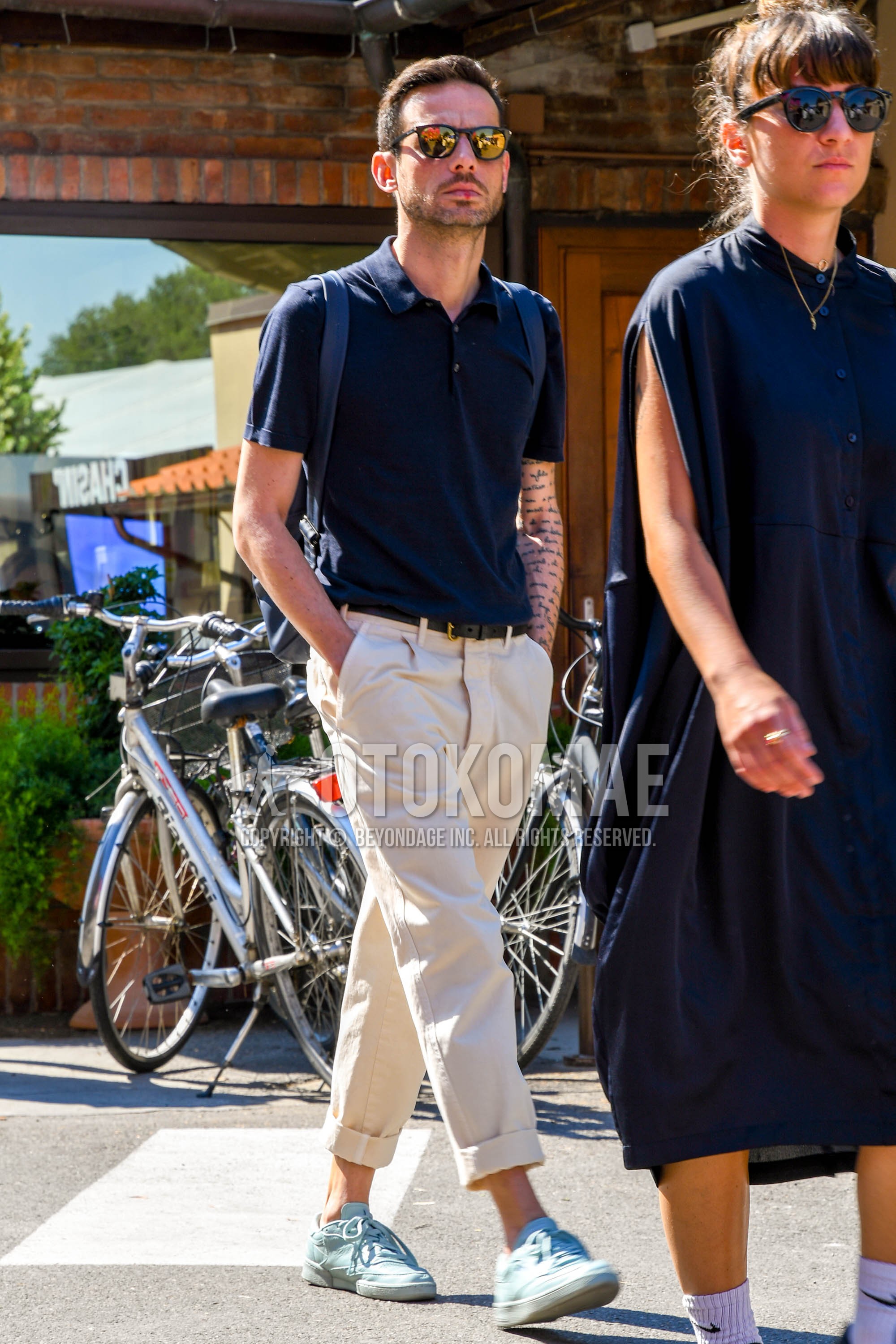 Men's summer outfit with plain sunglasses, navy plain polo shirt, black plain leather belt, beige plain cropped pants, plain chinos, light blue low-cut sneakers.