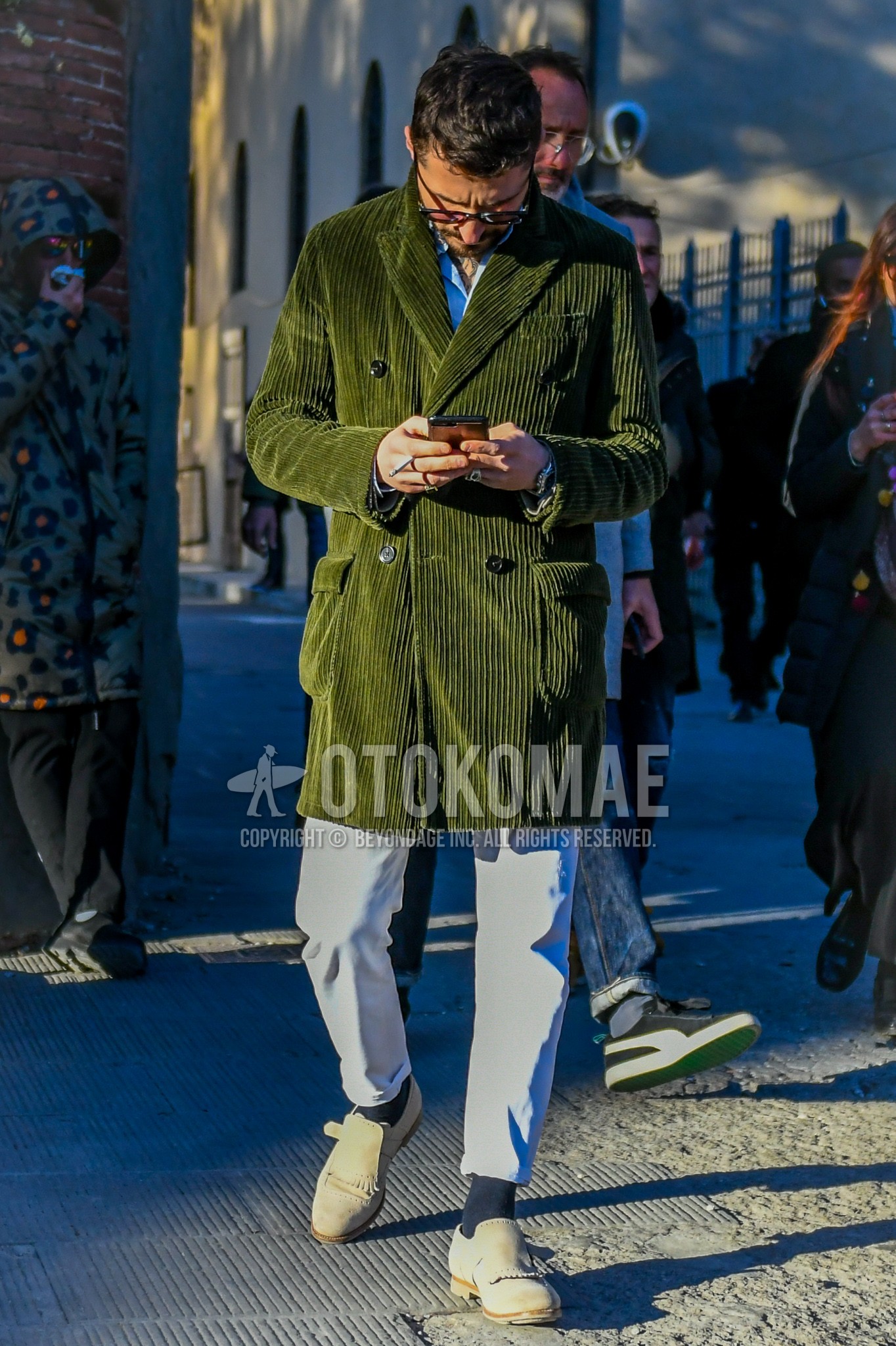 Men's autumn winter outfit with black plain glasses, olive green plain chester coat, light blue plain shirt, white plain cotton pants, navy plain socks, beige monk shoes leather shoes.