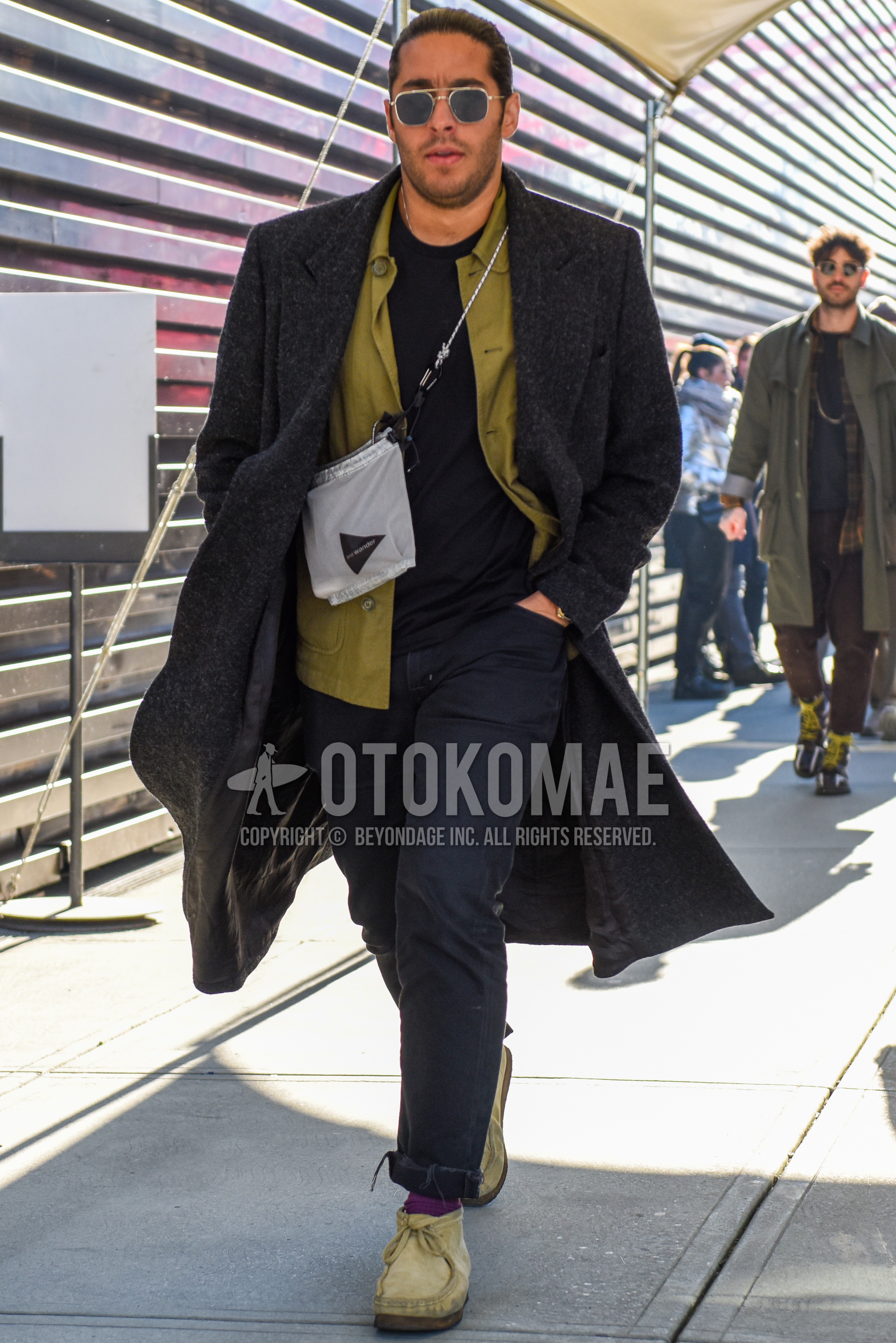 Men's autumn winter outfit with silver plain sunglasses, gray plain chester coat, olive green plain shirt jacket, black plain t-shirt, black plain denim/jeans, purple plain socks, beige chukka boots, silver one point shoulder bag.