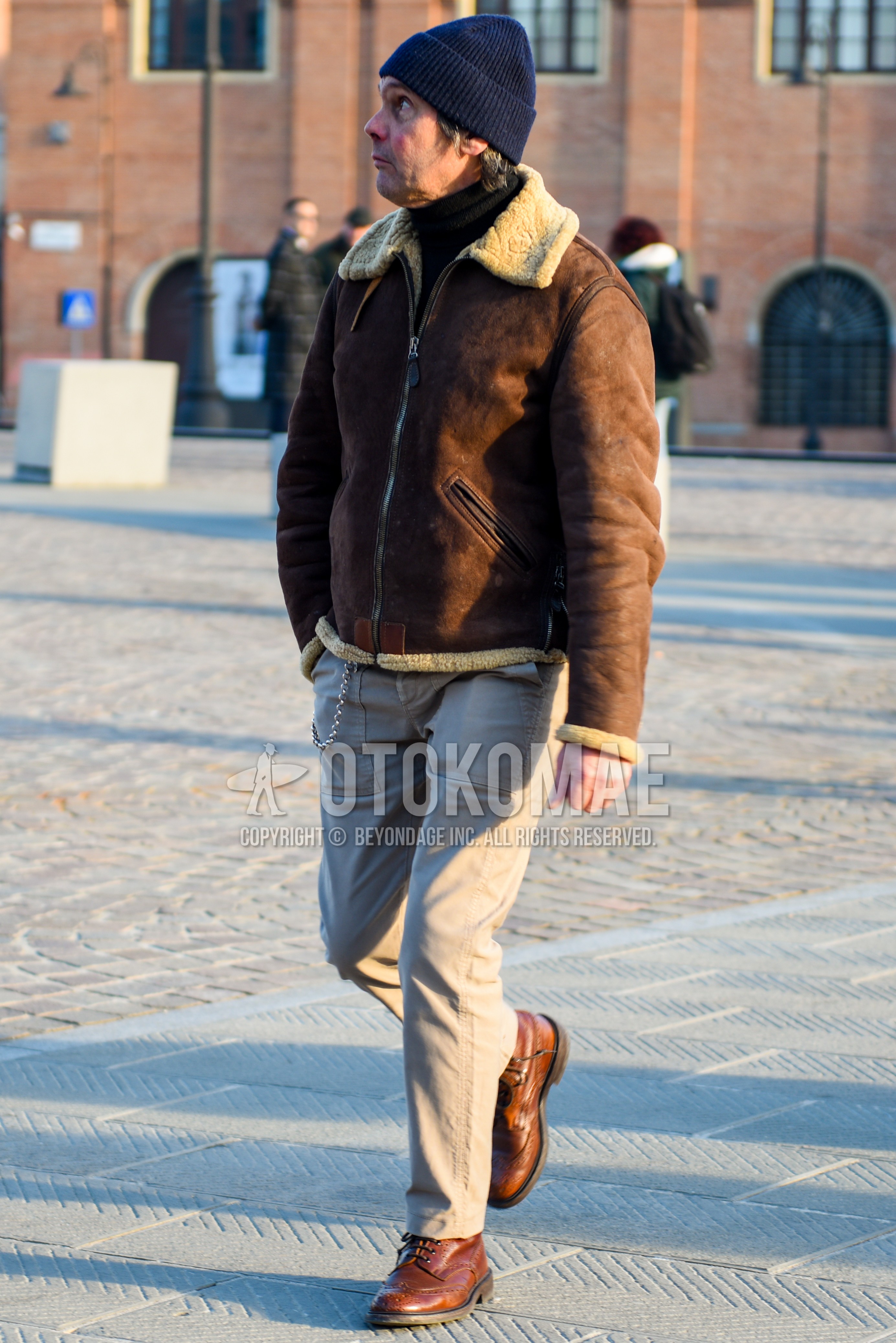 Men's autumn winter outfit with navy plain knit cap, brown plain leather jacket, black plain turtleneck knit, beige plain chinos, brown  boots.