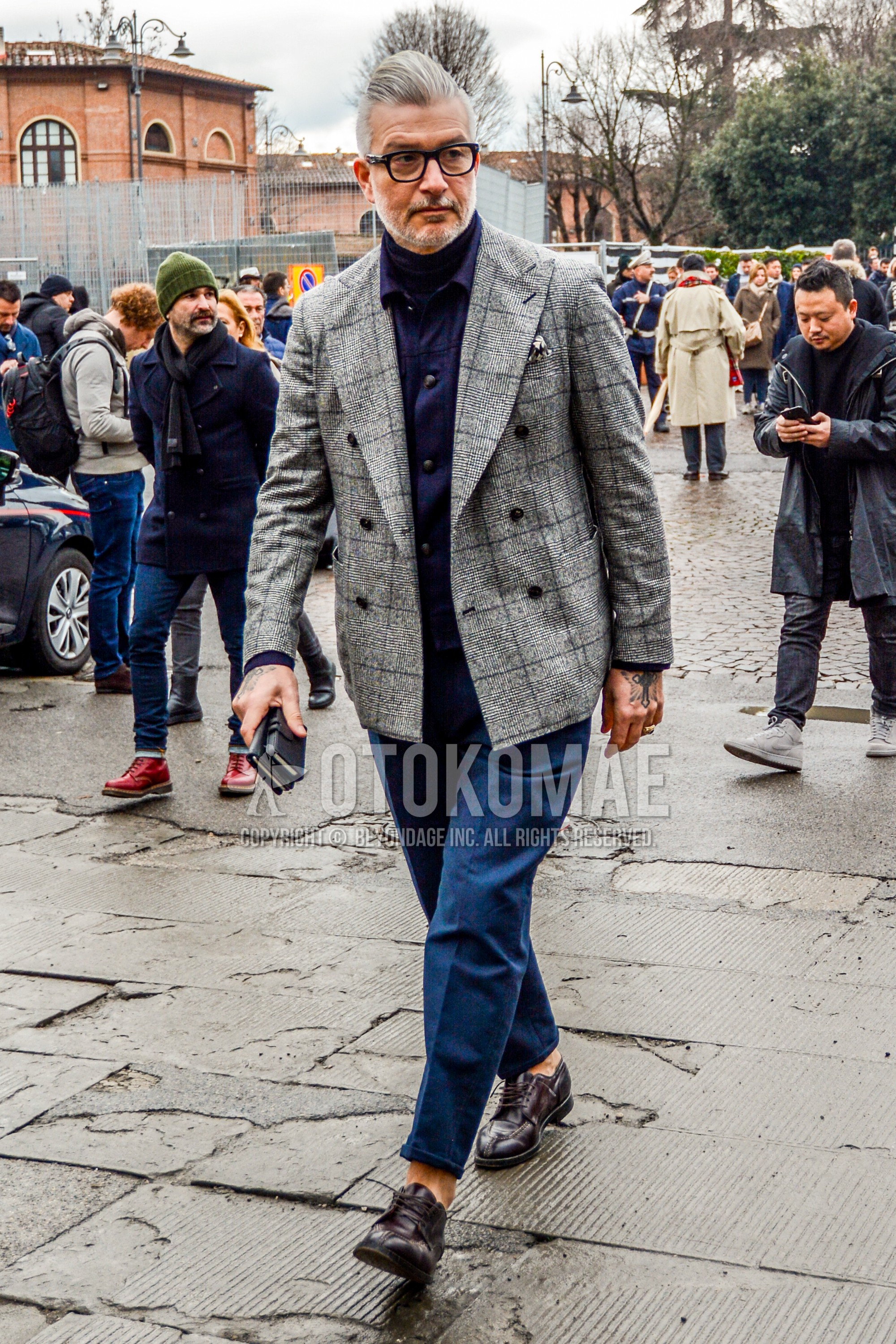 Men's winter outfit with plain glasses, gray check tailored jacket, navy plain shirt jacket, black plain turtleneck knit, blue plain ankle pants, brown u-tip shoes leather shoes.