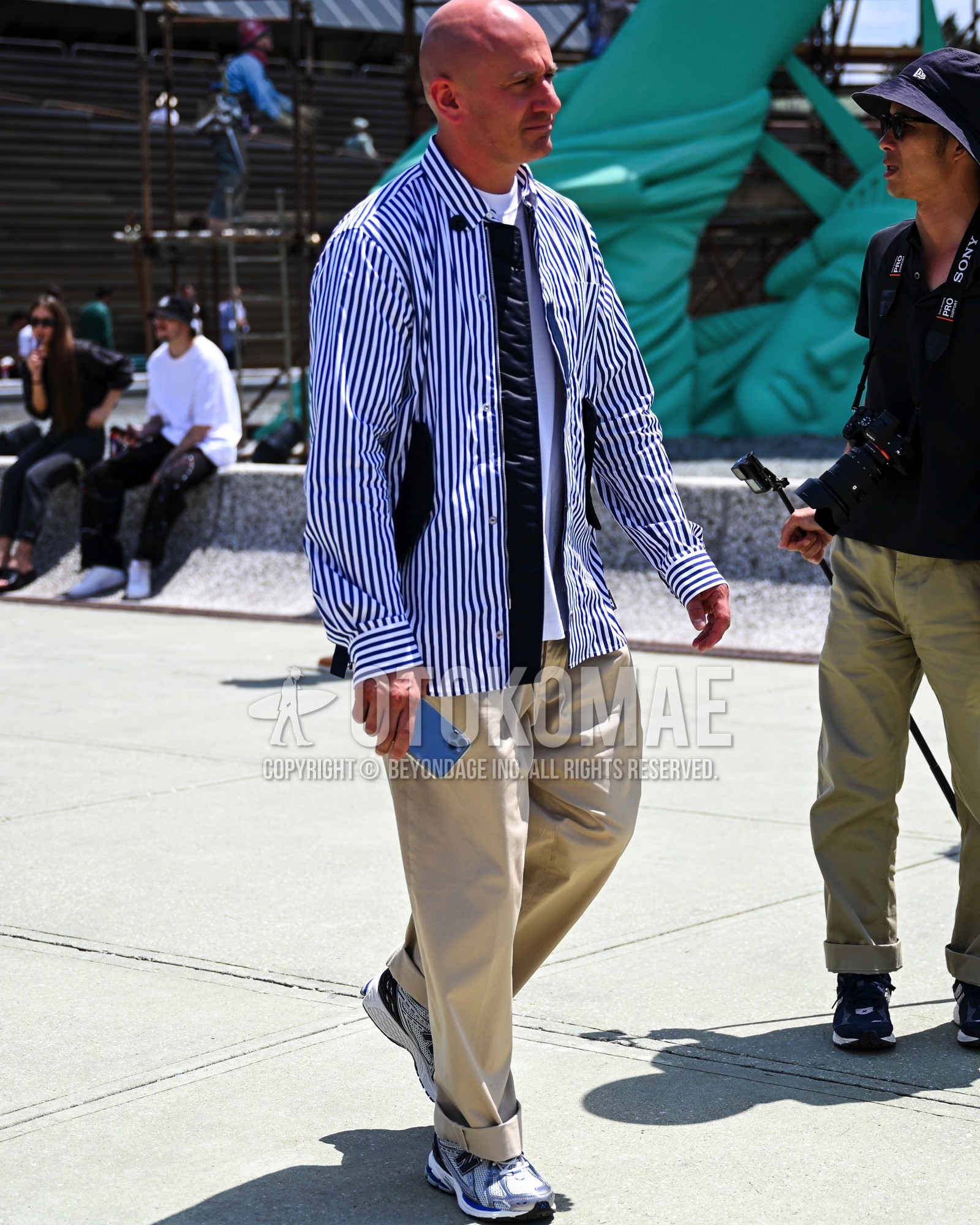 Men's spring summer autumn outfit with blue stripes shirt, white plain t-shirt, beige plain chinos, white low-cut sneakers.