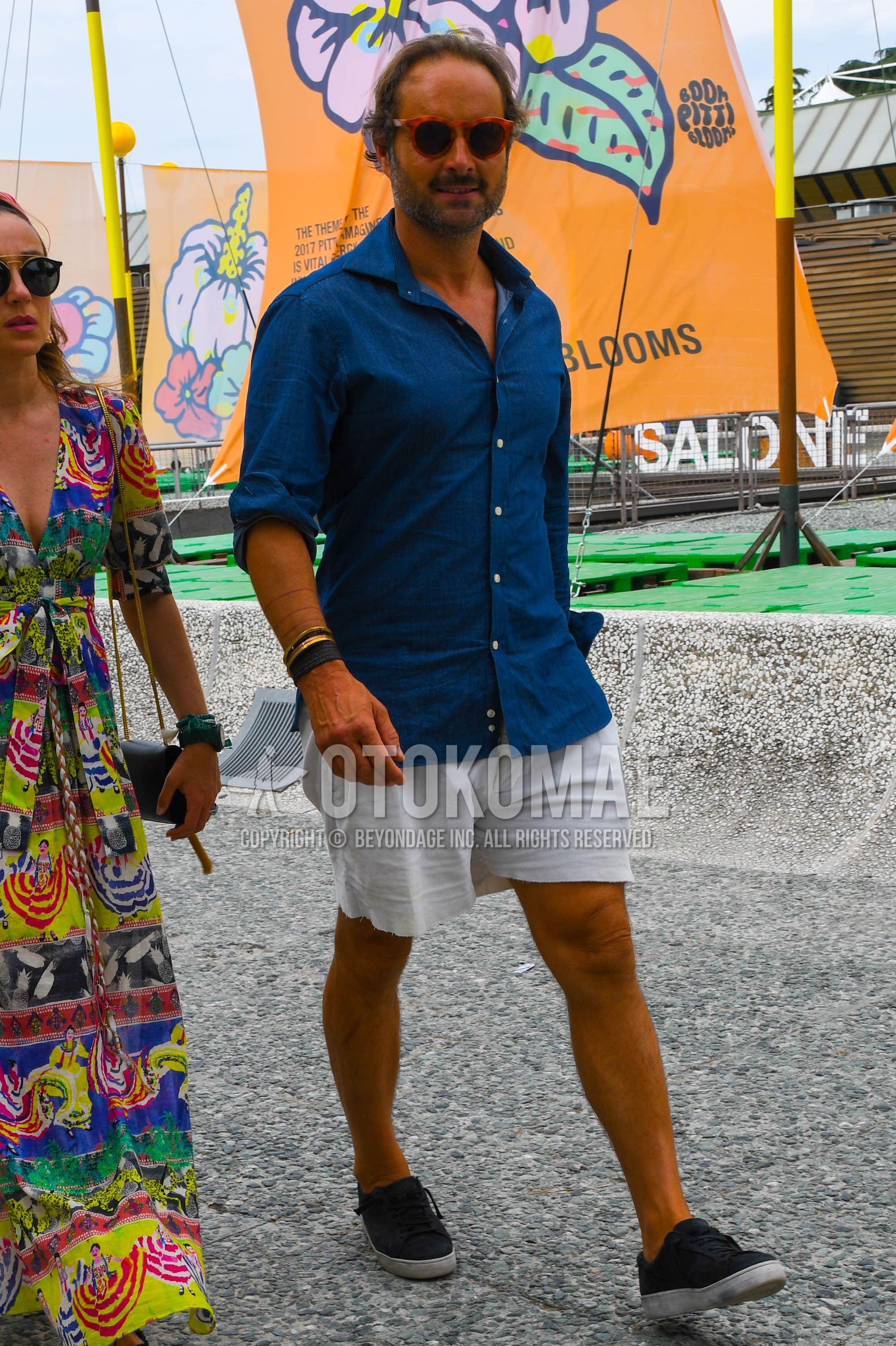 Men's summer outfit with tortoiseshell sunglasses, blue plain shirt, white plain short pants, black low-cut sneakers.