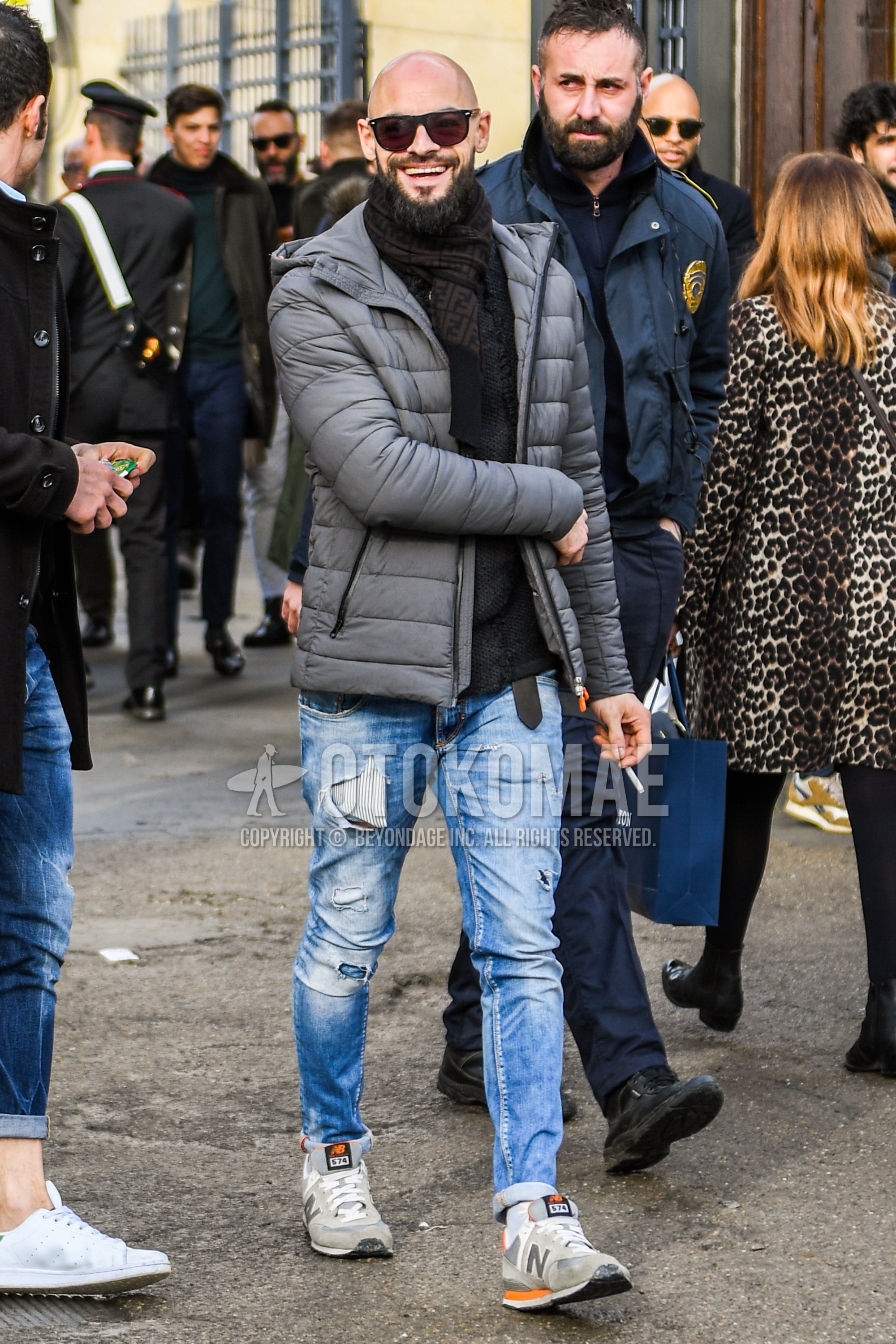 Men's autumn winter outfit with plain sunglasses, black brown scarf scarf, gray plain down jacket, blue plain damaged jeans, gray low-cut sneakers.